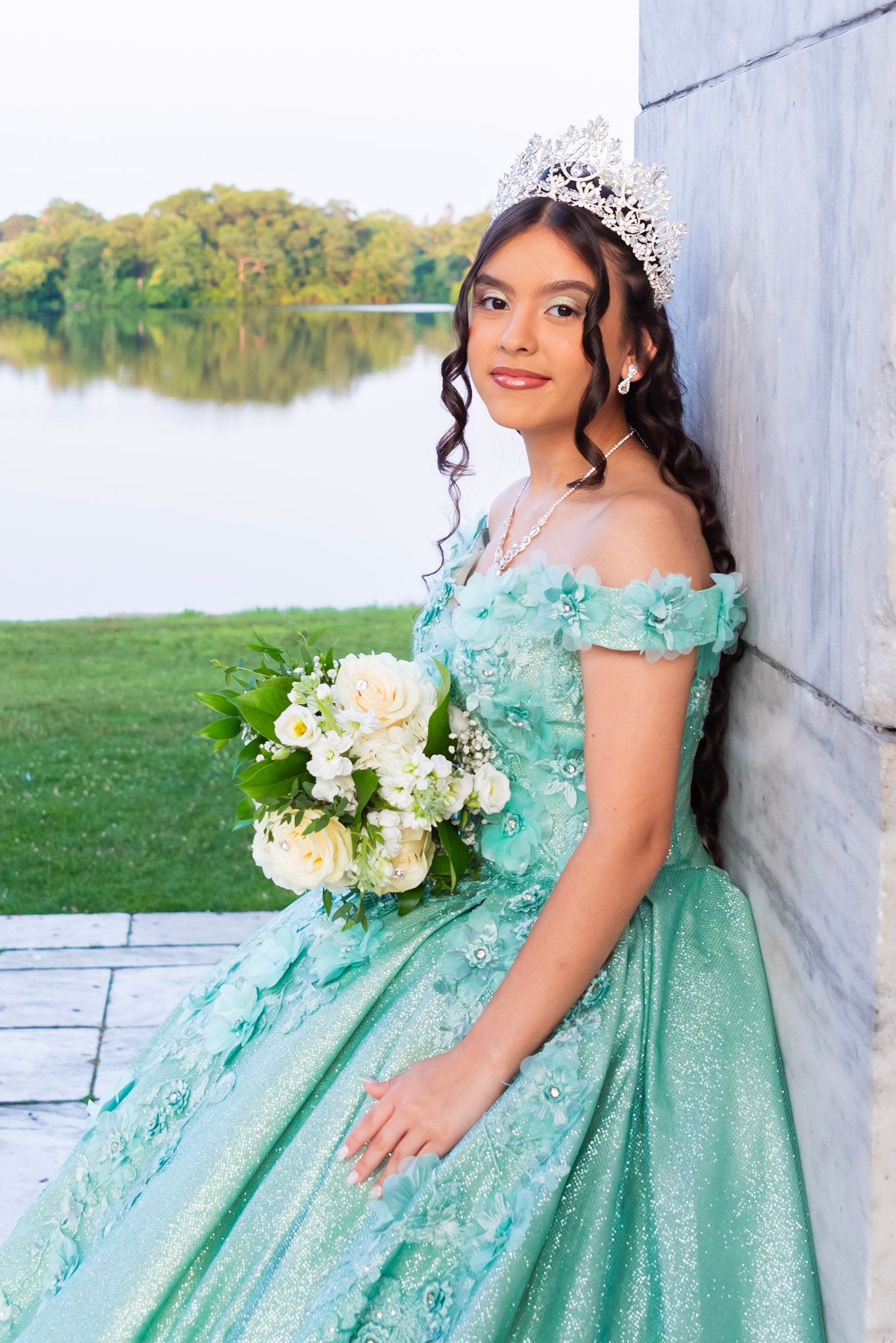 A mint green off-shoulder ballgown with lace details and white floral bouquet photographed by a lakeside.