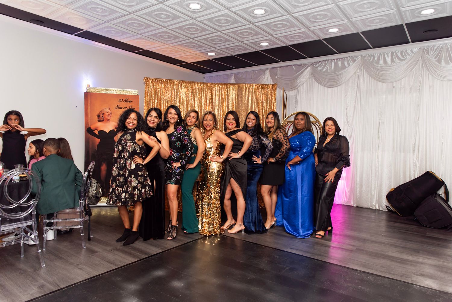 Large group photo of formal event attendees posing together in elegant white-walled venue.