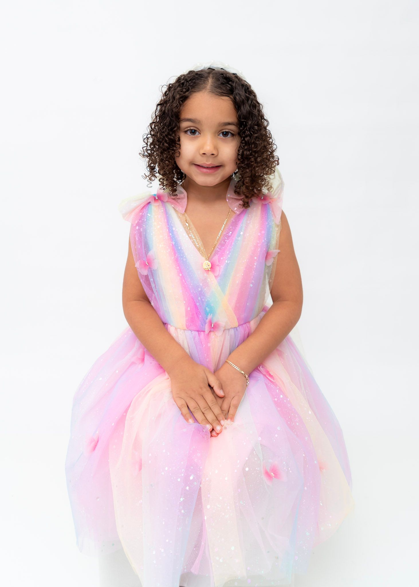 A pastel rainbow dress sparkles against a white studio background in a series of portrait shots.