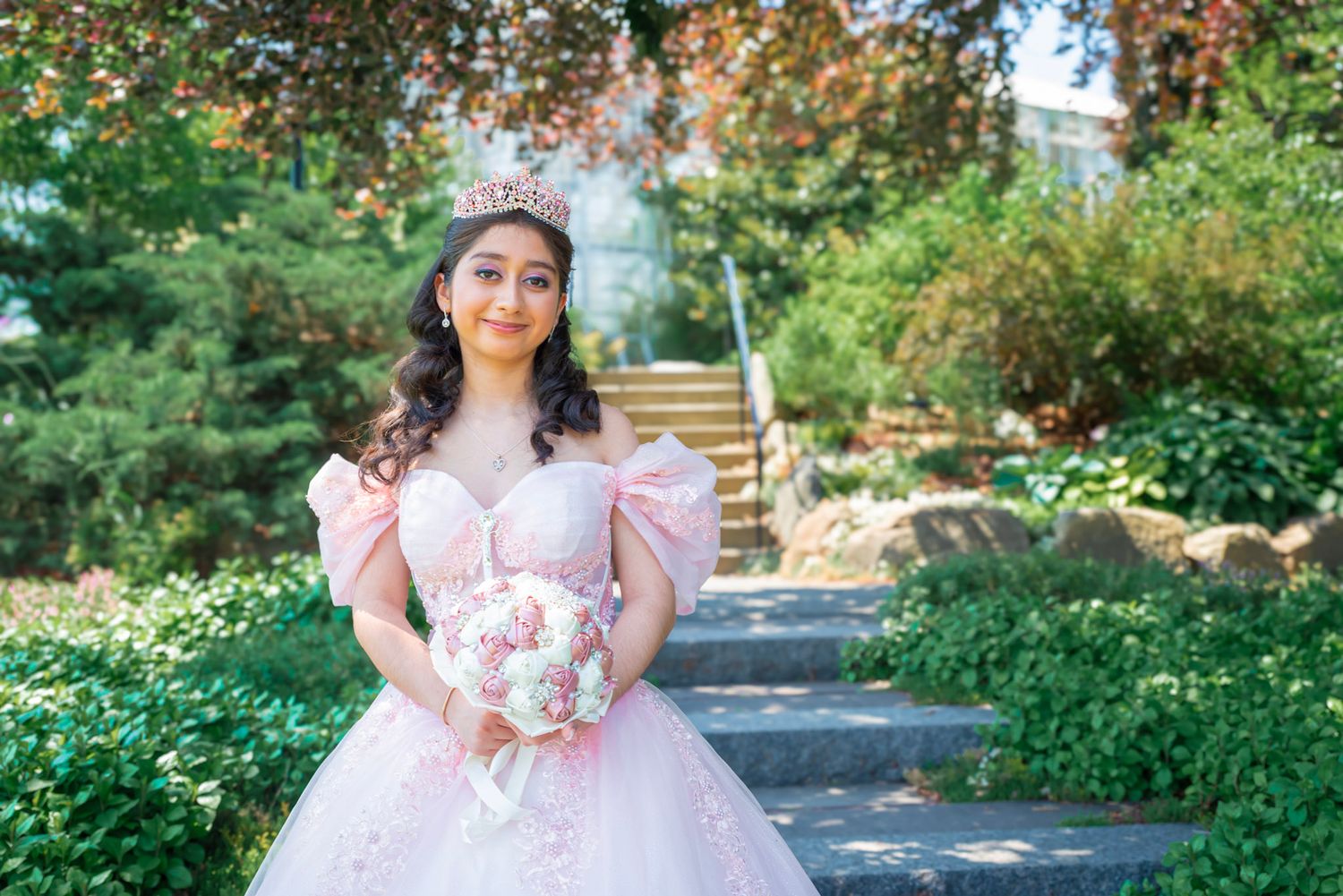 Young girl in a pink princess dress posing in a lush garden setting during a photo session.