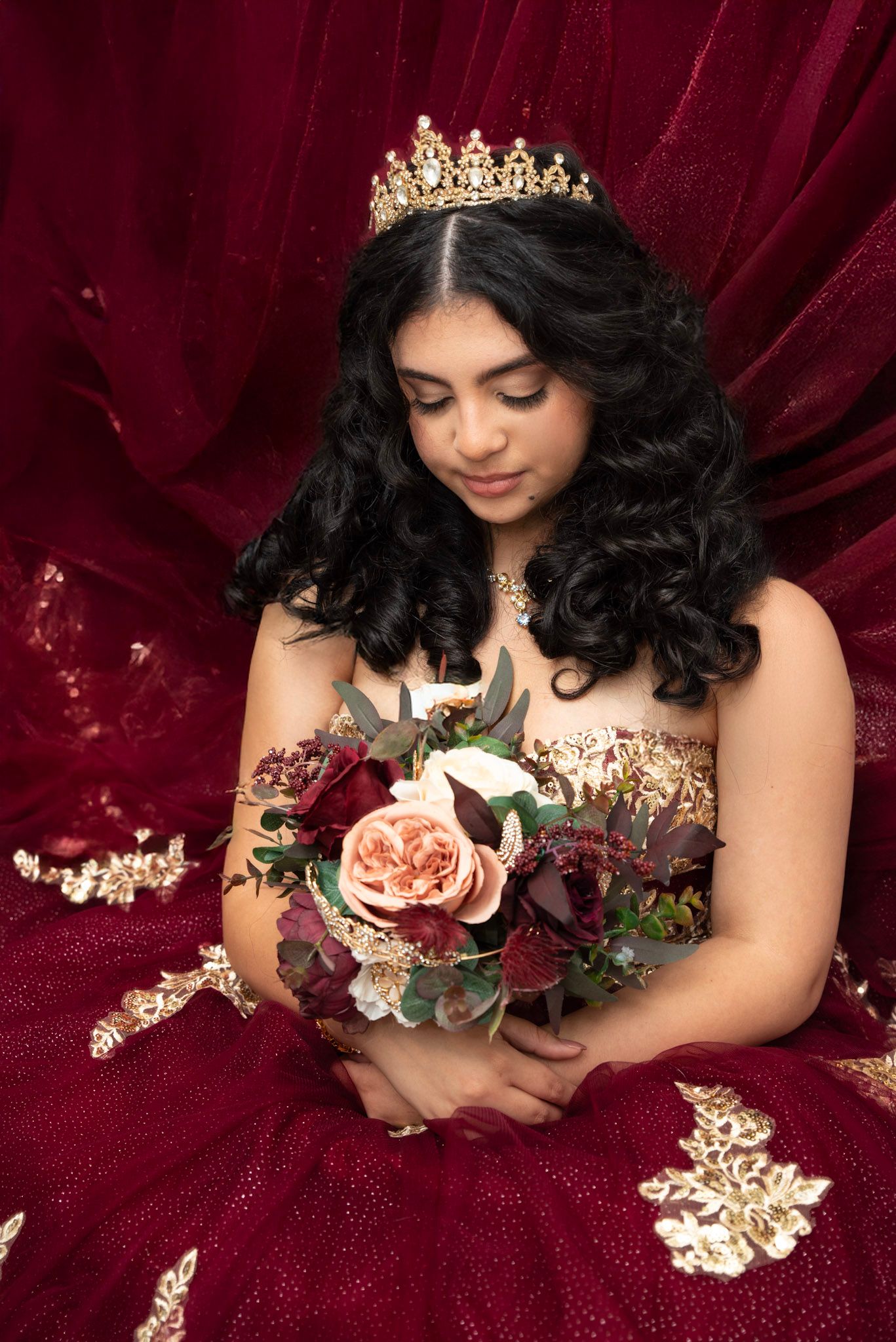 Romantic portrait with crown and flowers against rich burgundy velvet backdrop.