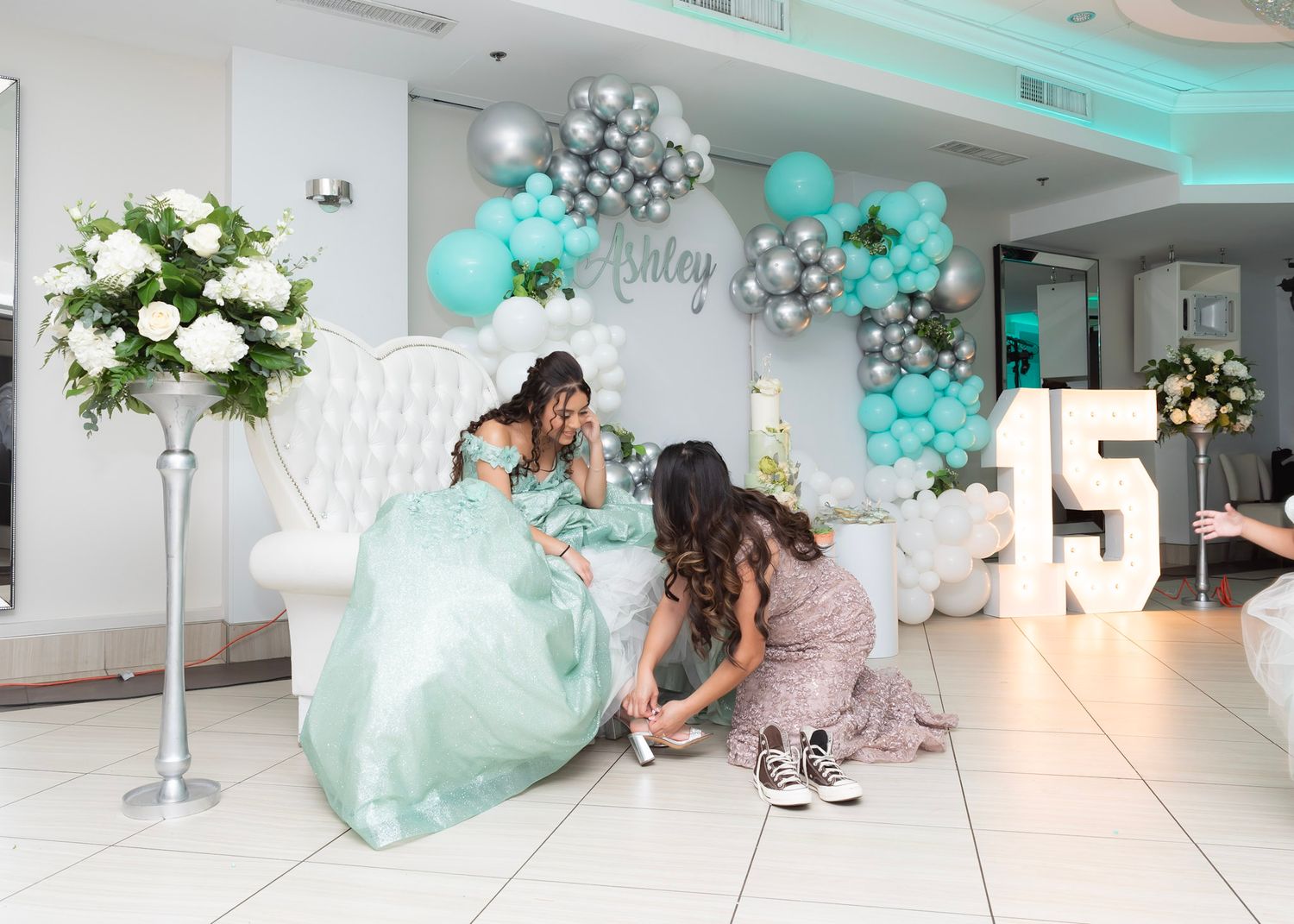 Baby shower celebration space decorated with teal and silver balloons and white floral arrangements.