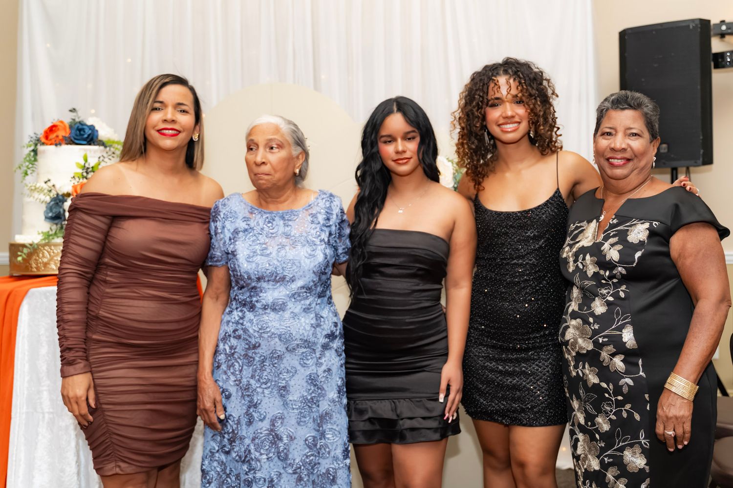 A group of people dressed in formal attire pose together against a white wall at a social gathering.