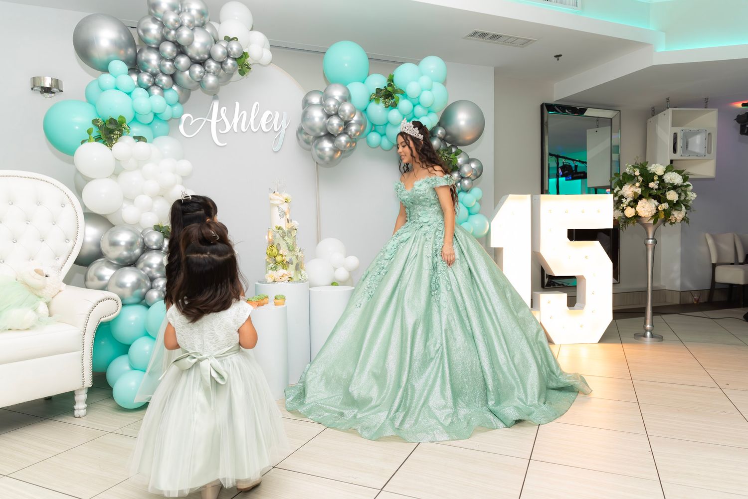 Modern event space with teal balloon arch and white furniture for celebration.