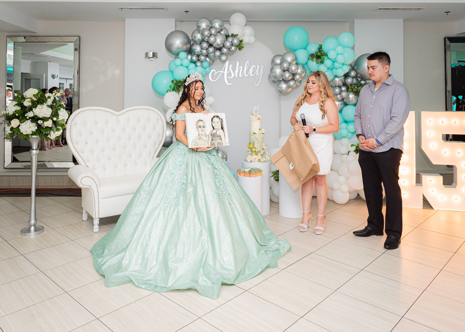 A celebration in a white ballroom decorated with mint green and silver balloons for a special occasion.