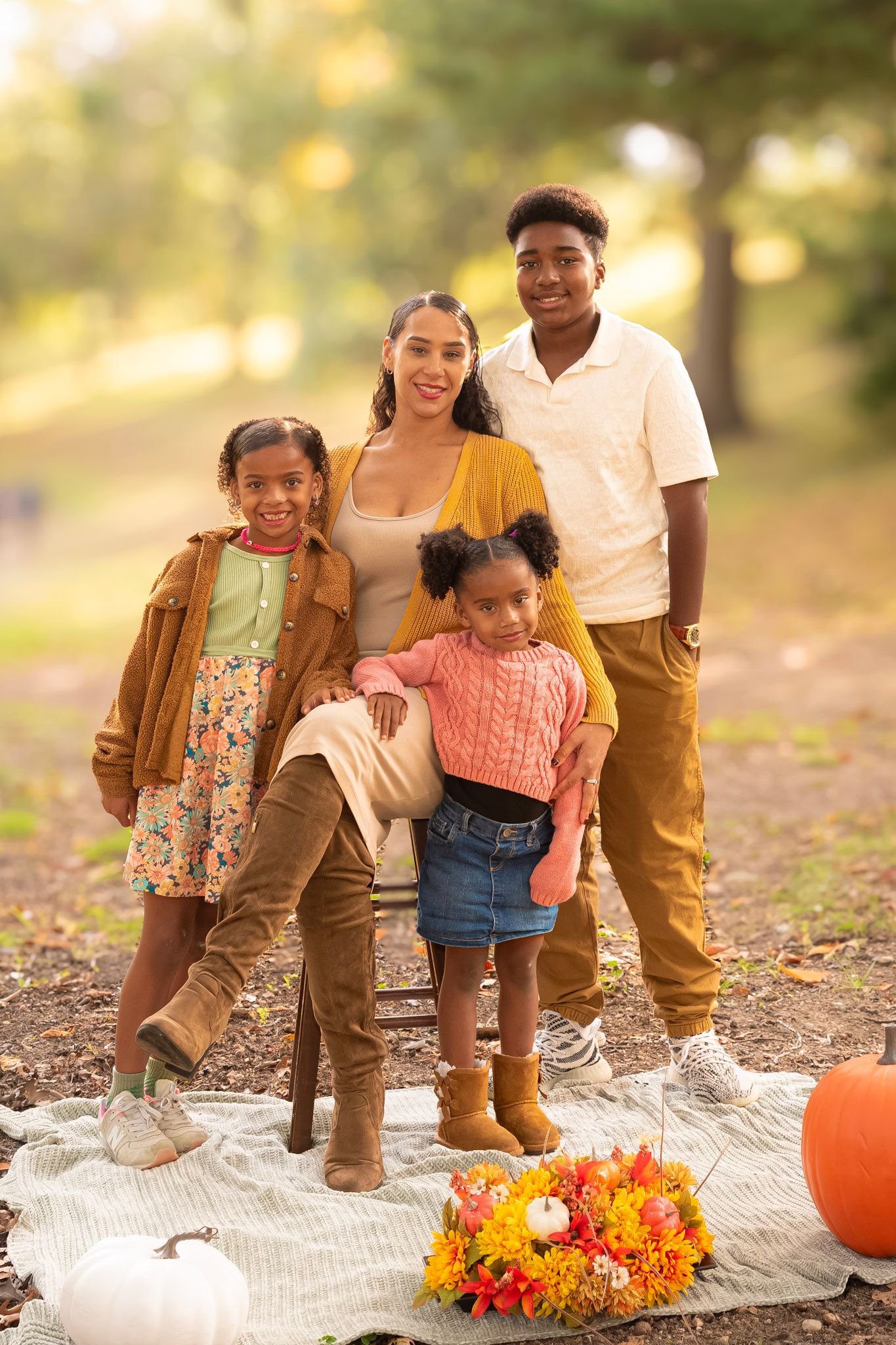 A cozy autumn family photo session outdoors with pumpkins and a floral wreath on a blanket at sunset.