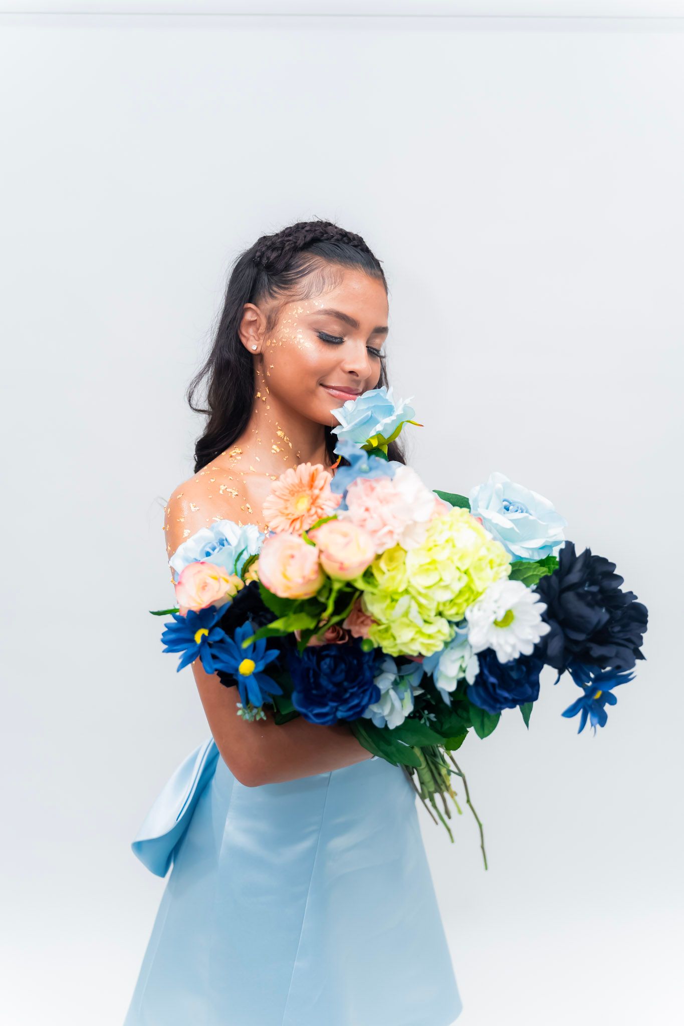 Woman in off-shoulder dress holding colorful floral arrangements against white background in artistic photo series.