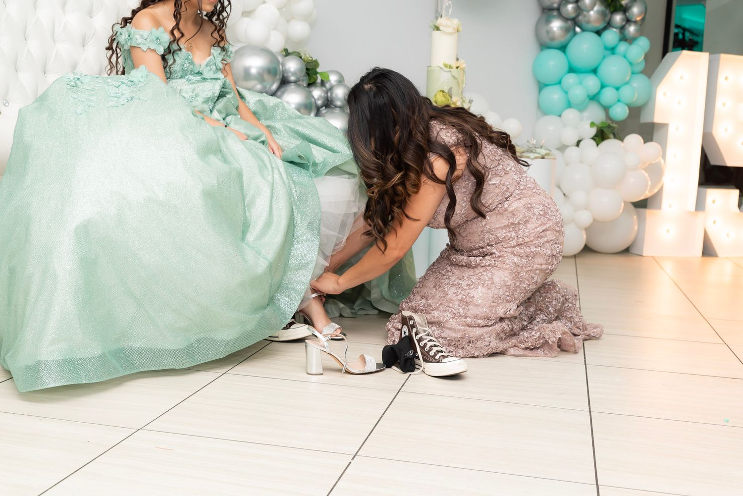 A person in a mint green dress sits on the floor near teal balloons and gift bags at a party.