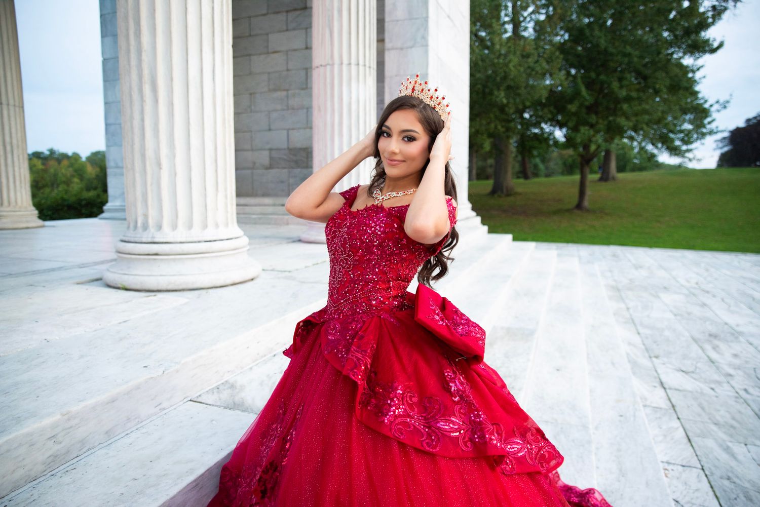Elegant portraits in a red ball gown among classical white columns.