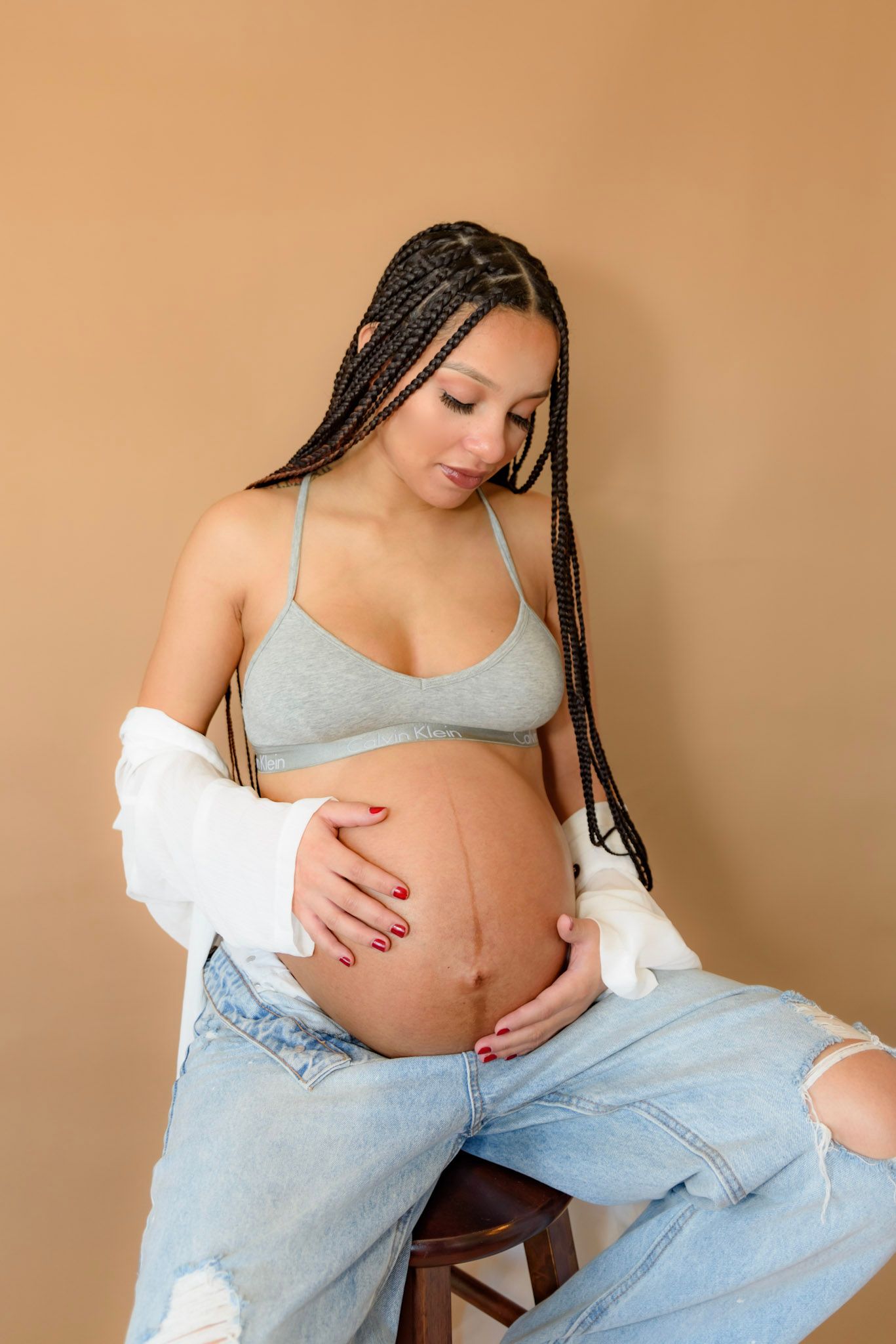 Maternity photo session featuring casual denim and white outfit against warm brown backdrop.