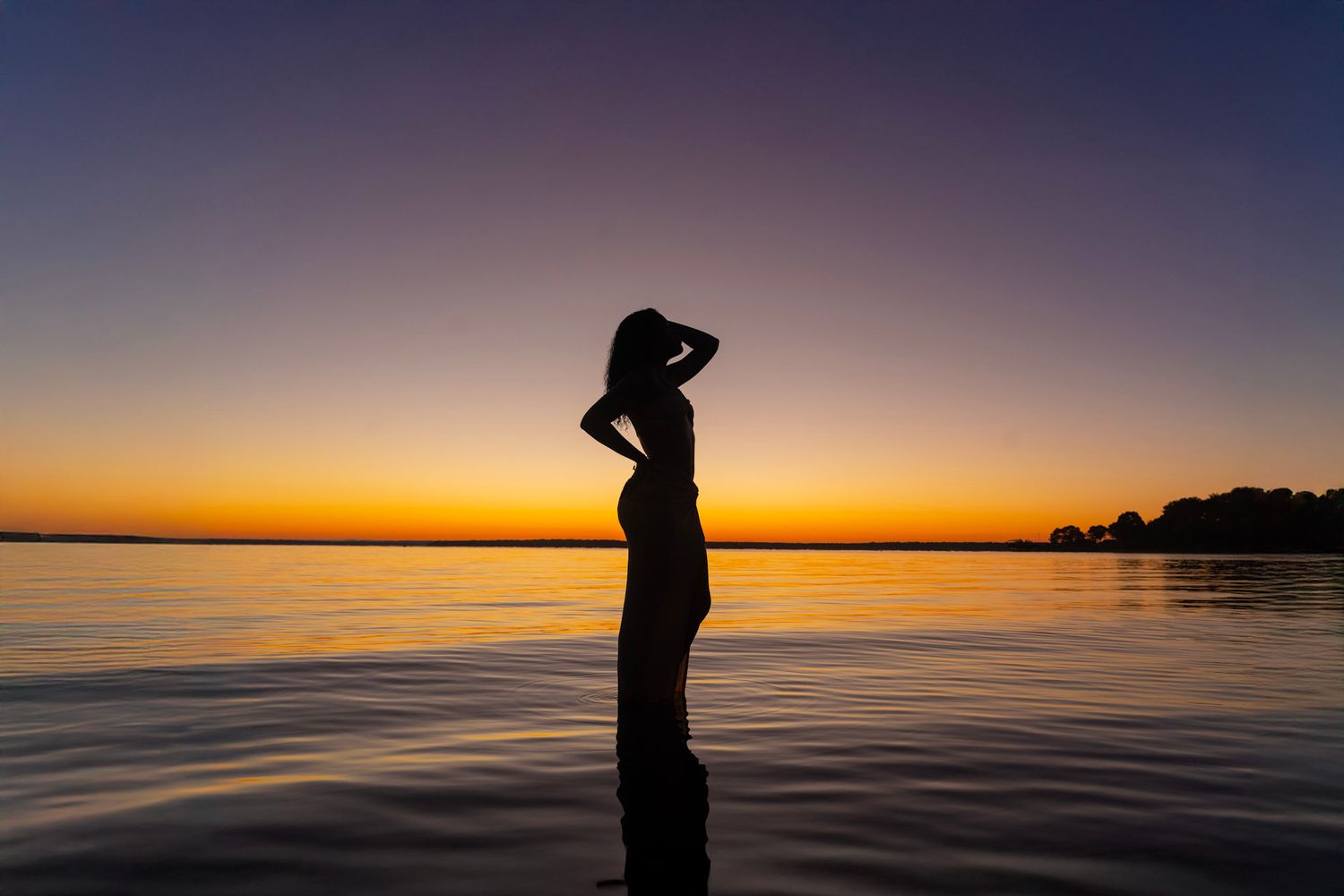 Silhouettes against a vibrant orange and purple sunset over calm ocean waters.