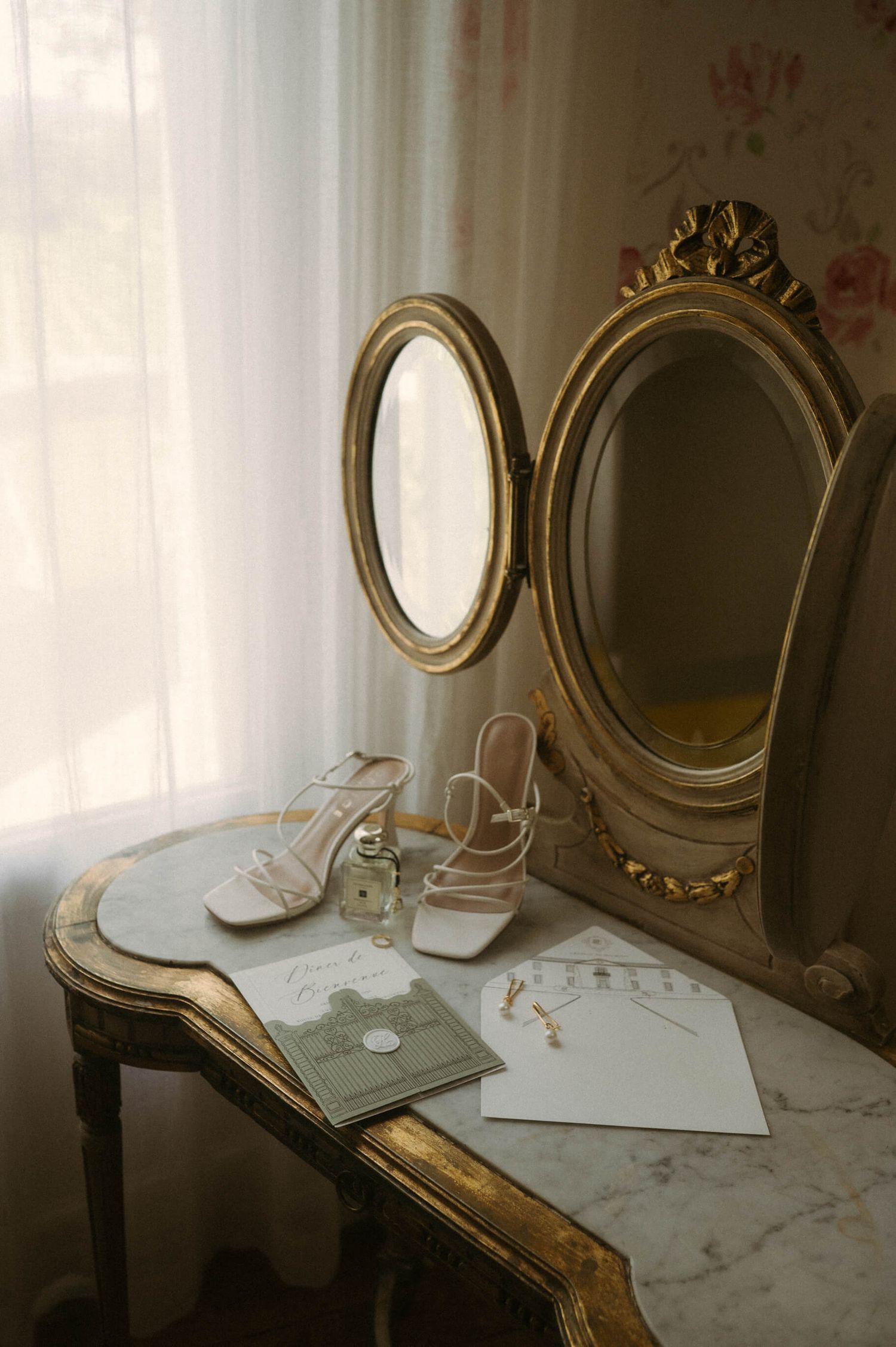 Vintage vanity table with ornate gold mirrors and wedding accessories in soft natural light.