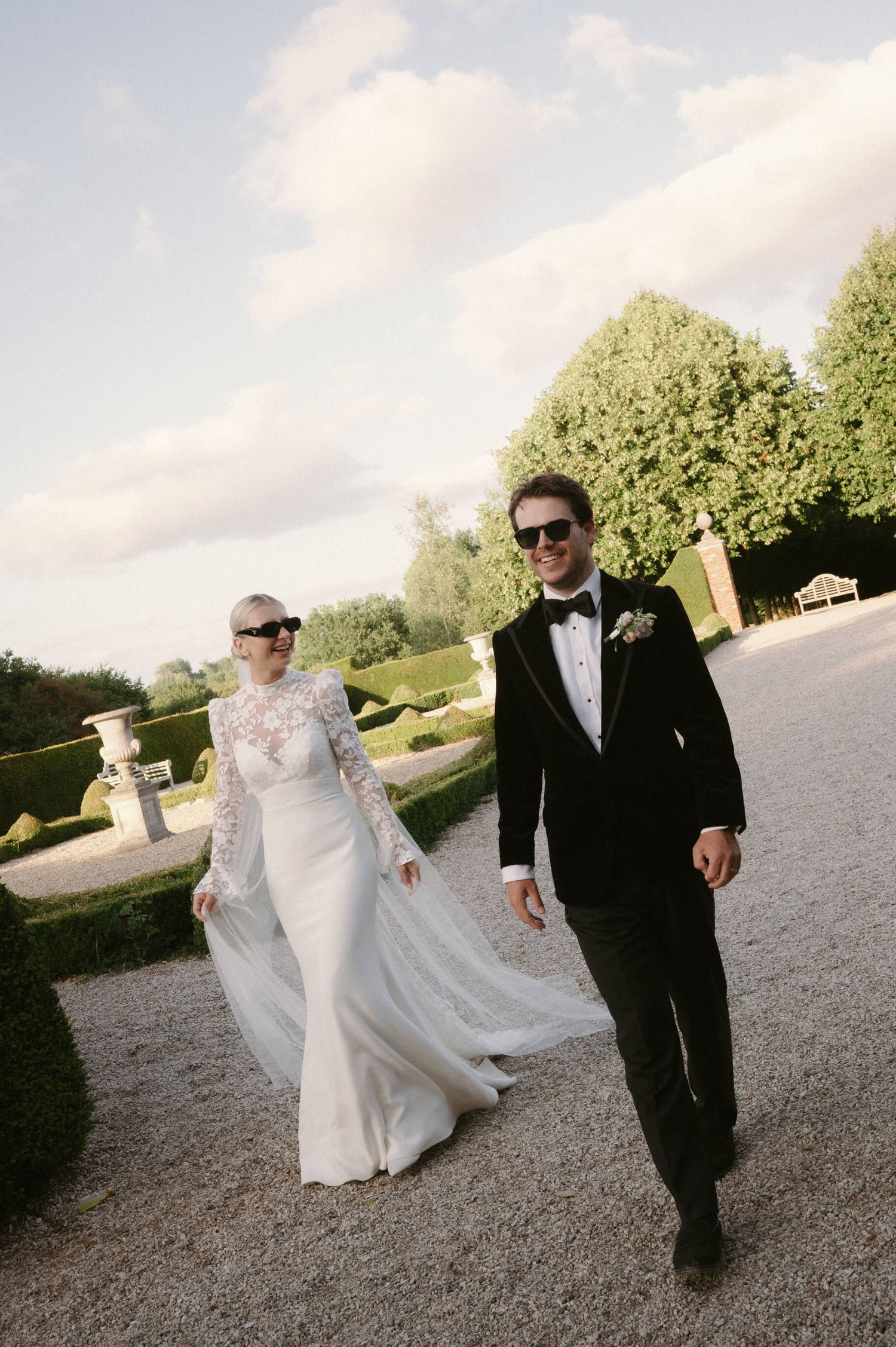 Couple walking together outdoors on a sunny day, with bride wearing flowing white dress.