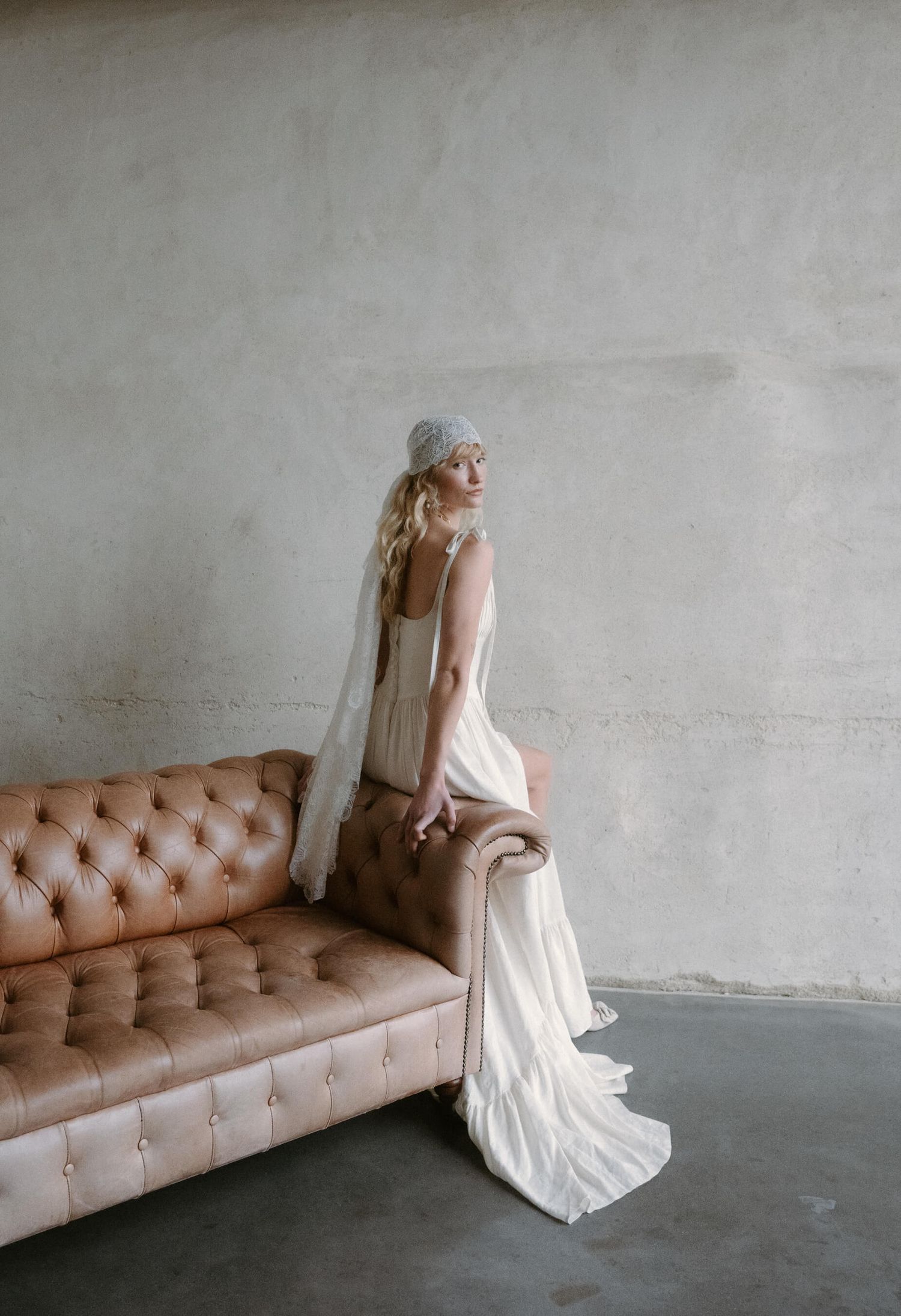 Bridal fashion shoot with vintage leather couch against concrete wall.