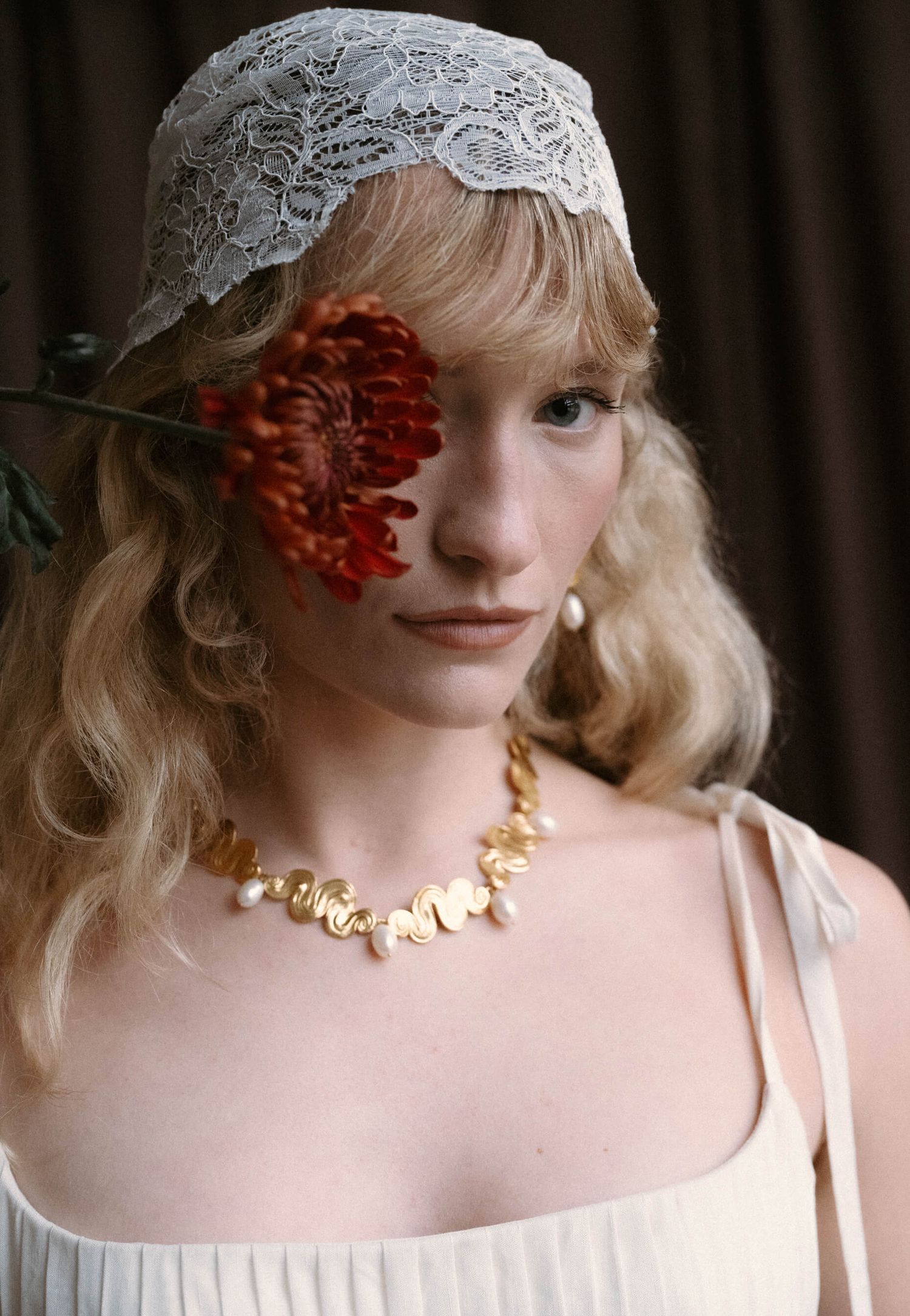 Vintage-inspired bridal portrait featuring delicate lace headpiece, red flower accent, and gold necklace details.