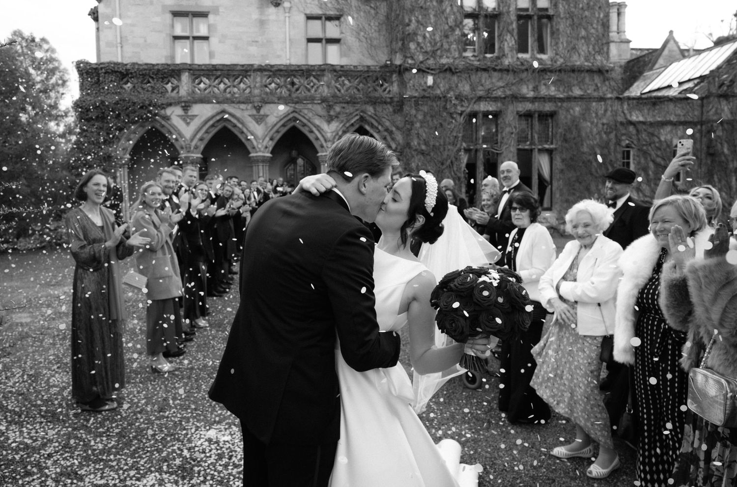 A black and white wedding photo collage showing various moments from a celebration at a historic stone building.