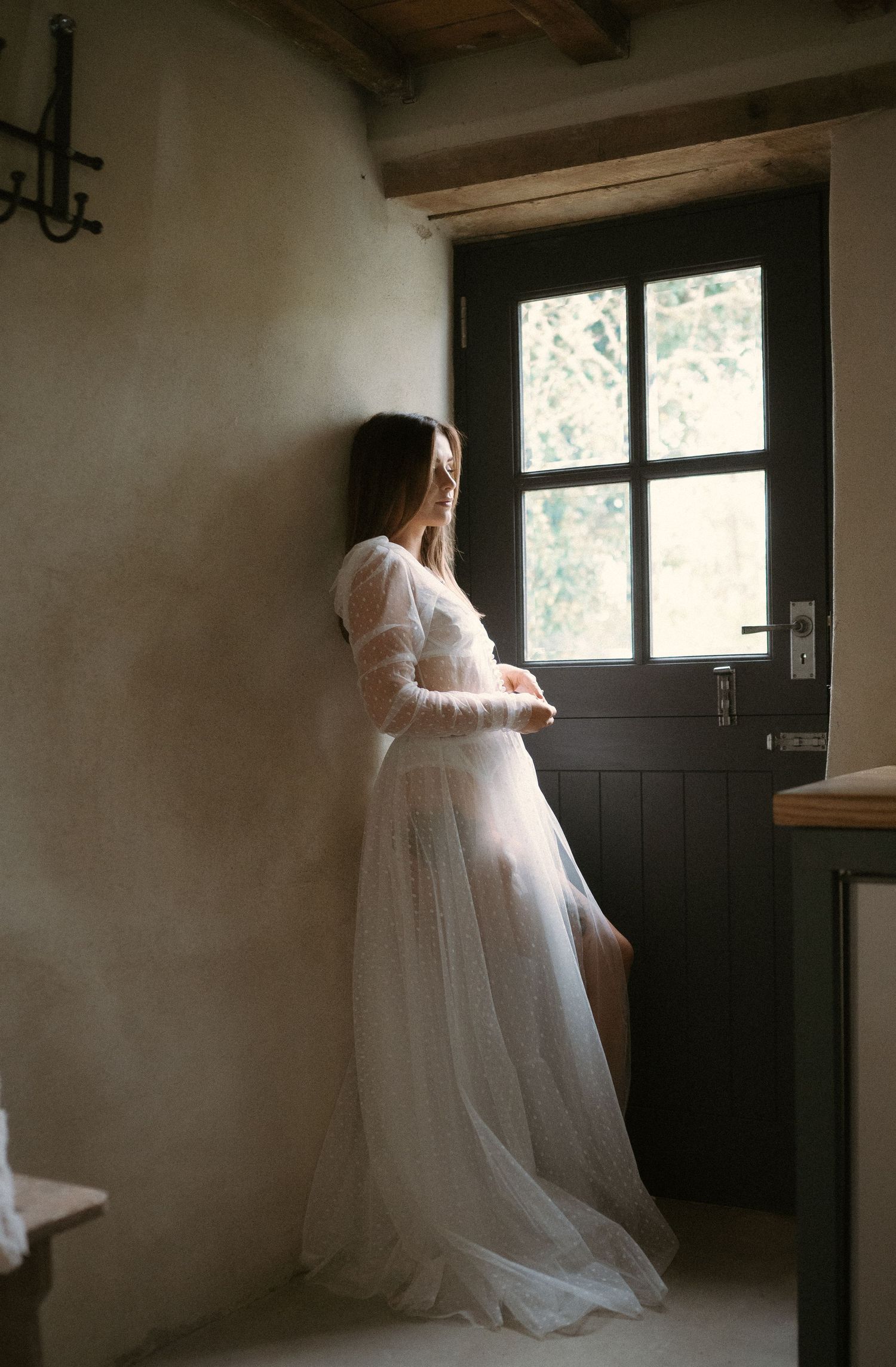 Dreamy bridal portrait by a rustic window in flowing white dress.