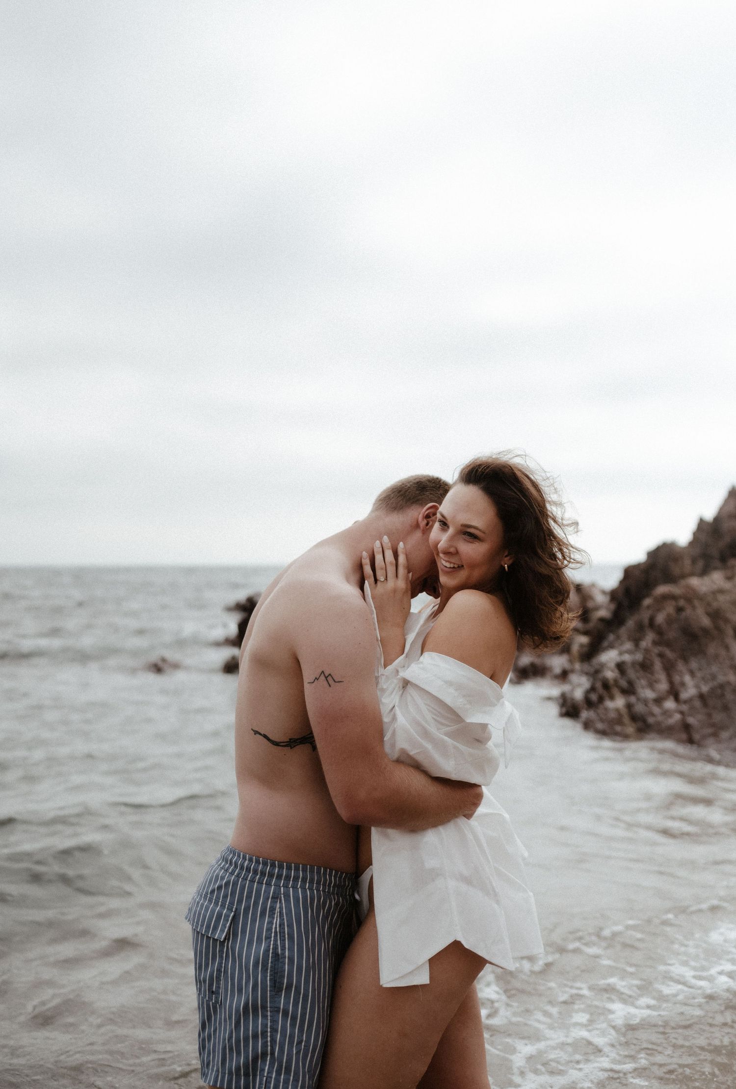 A romantic seaside photoshoot with waves crashing against rocky shore.