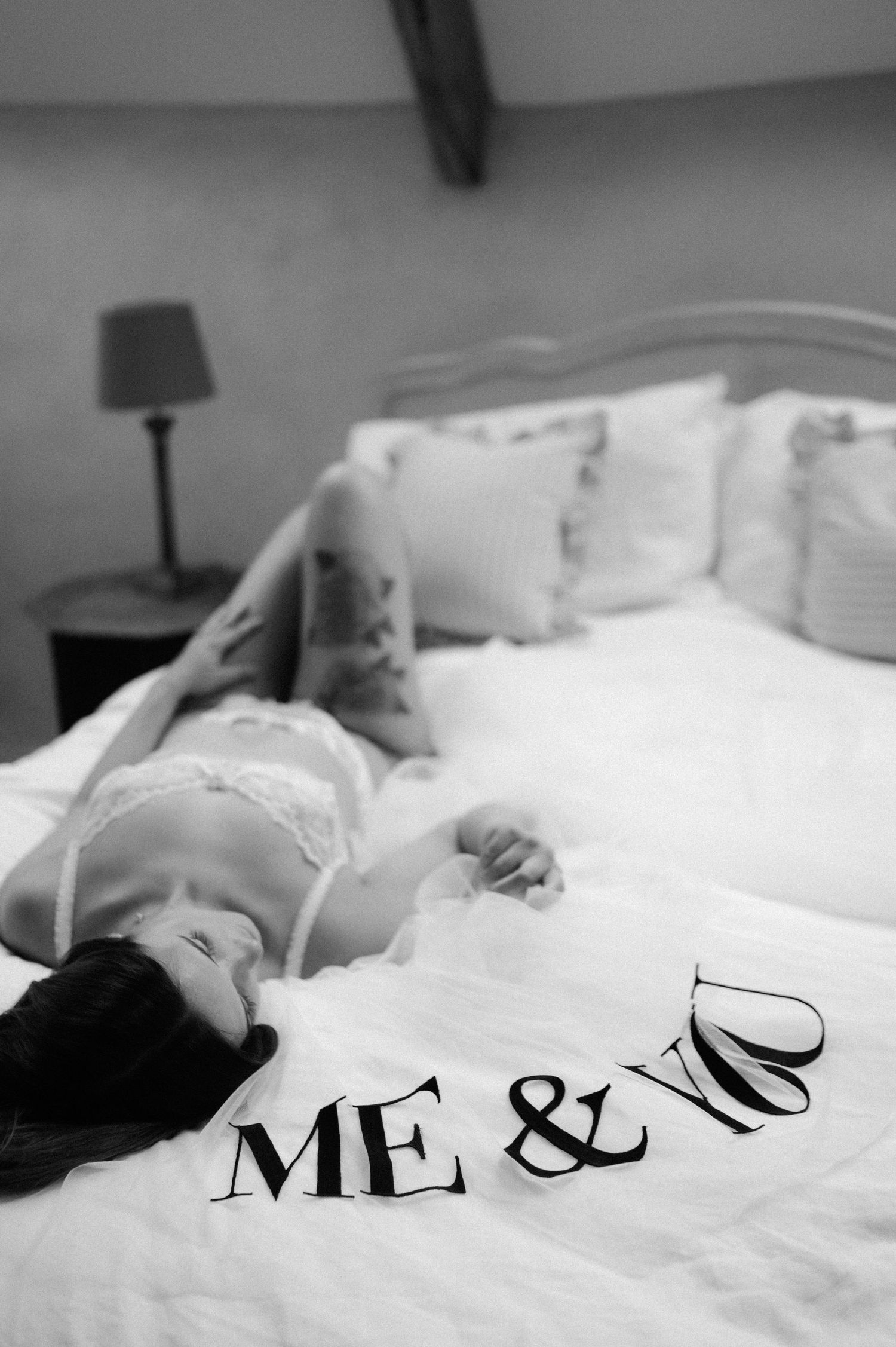 Black and white boudoir photo with 'ME &' text on white bedding.