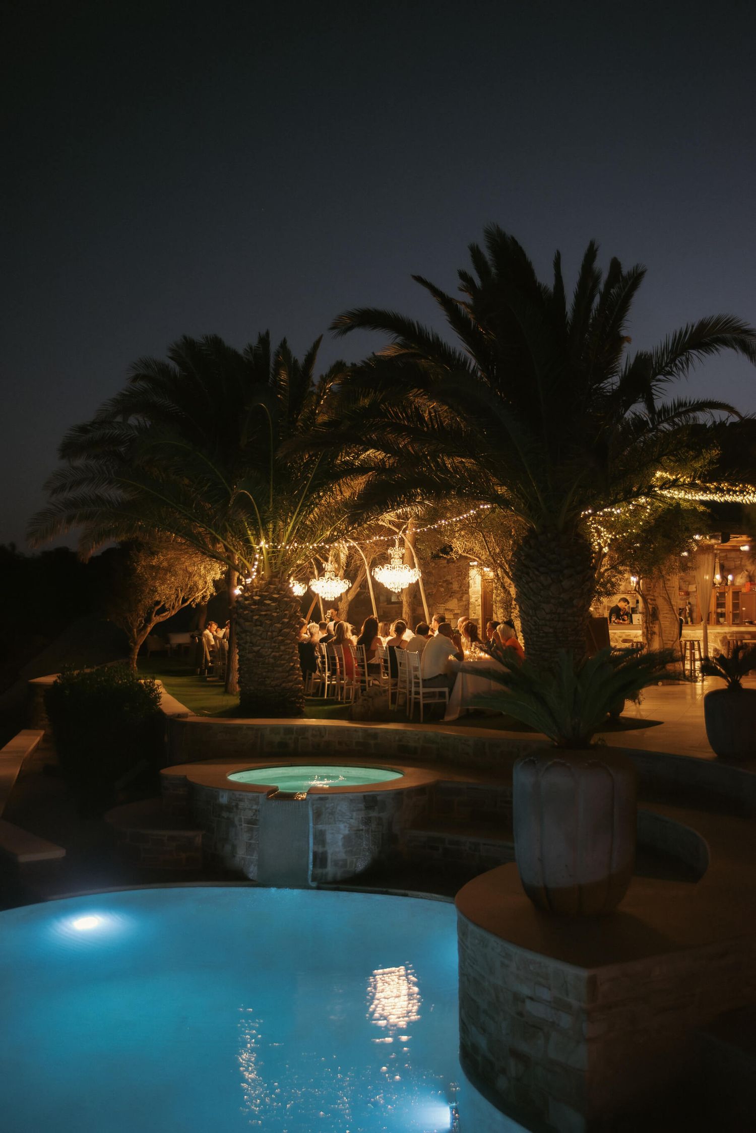 Evening poolside wedding reception with palm trees and string lights creating a romantic ambiance.