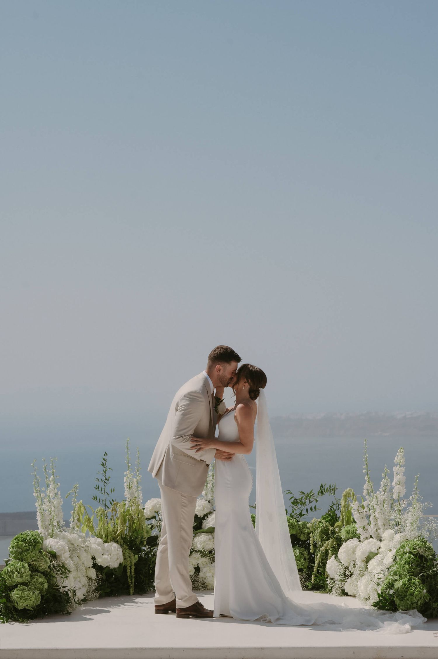An intimate wedding ceremony setup with white flowers against an ocean backdrop.