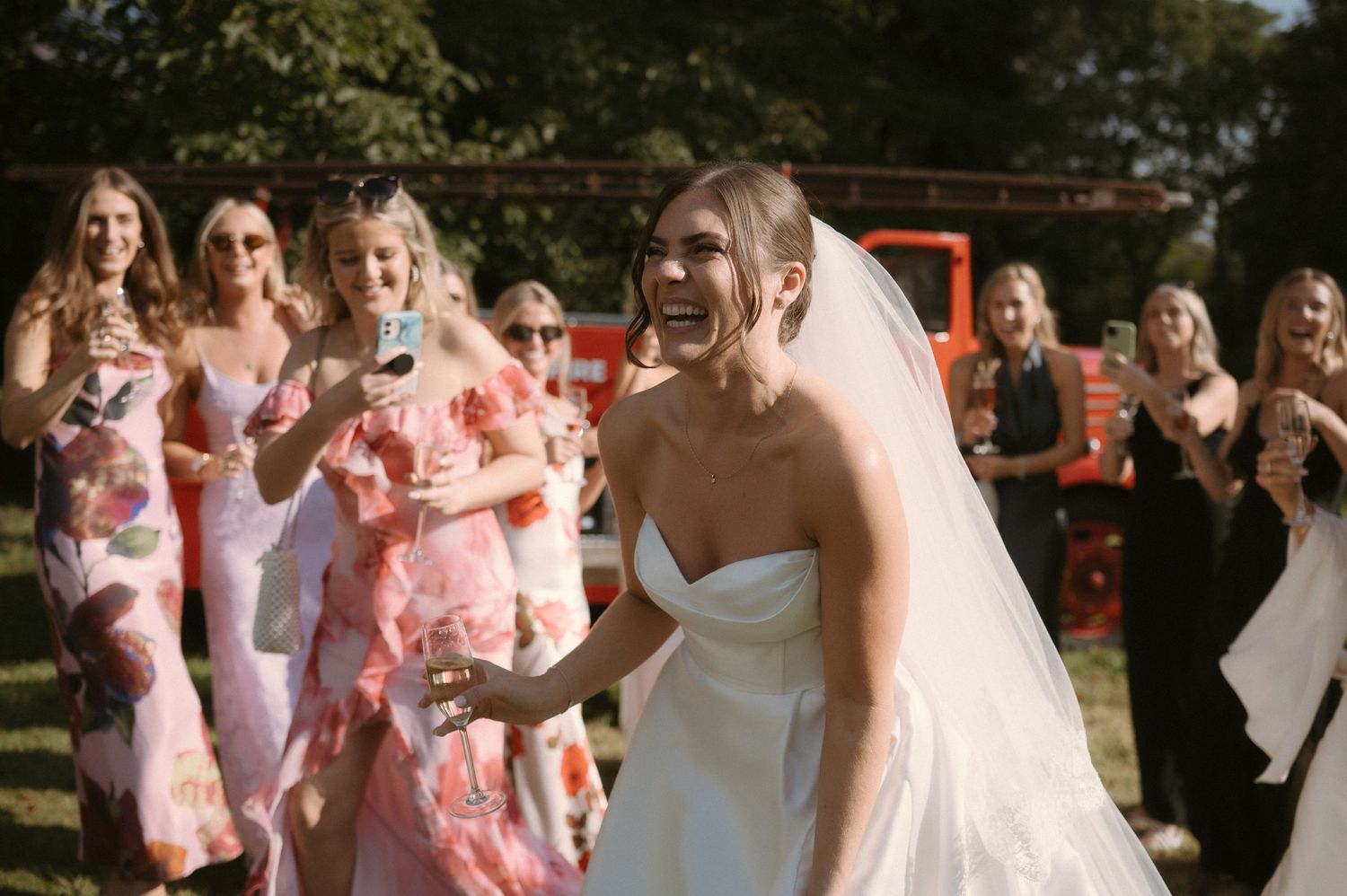 A joyful wedding celebration outdoors with bridesmaids wearing pink floral dresses.