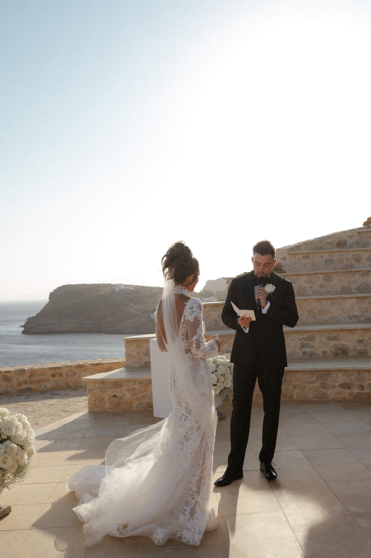 Romantic wedding couple dancing on a stone terrace overlooking a coastal landscape.
