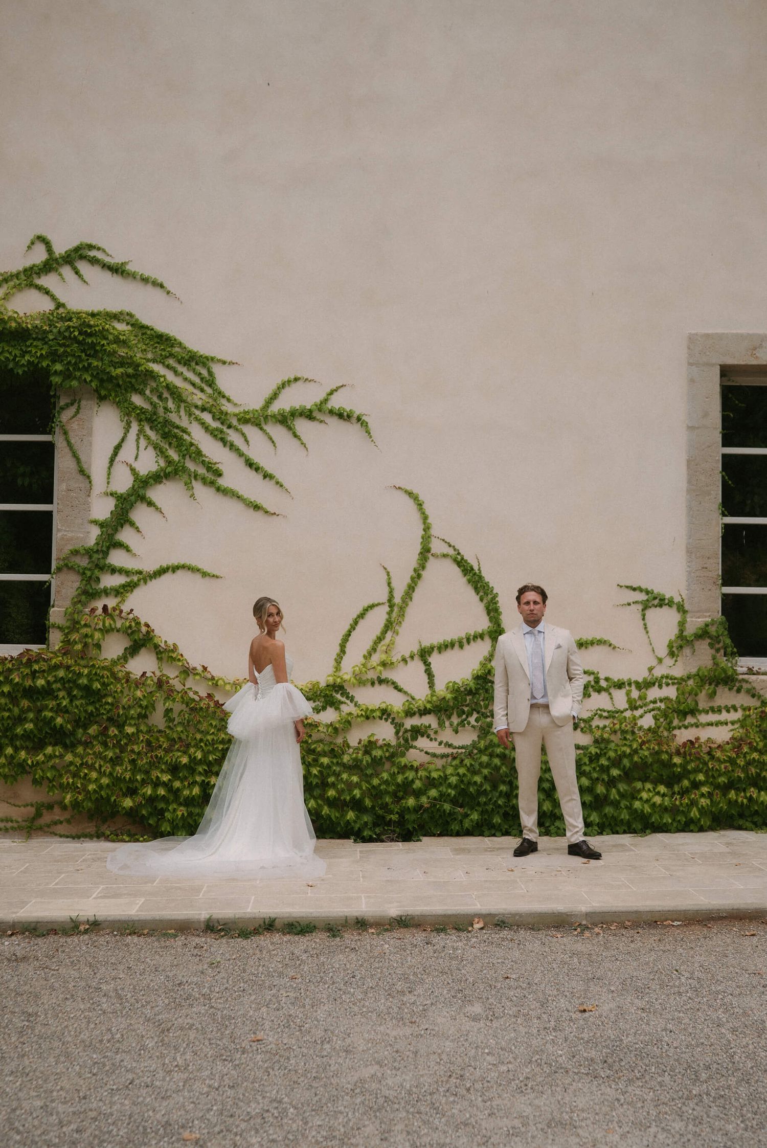 Artistic wedding portrait against white Mediterranean villa wall with climbing plants.