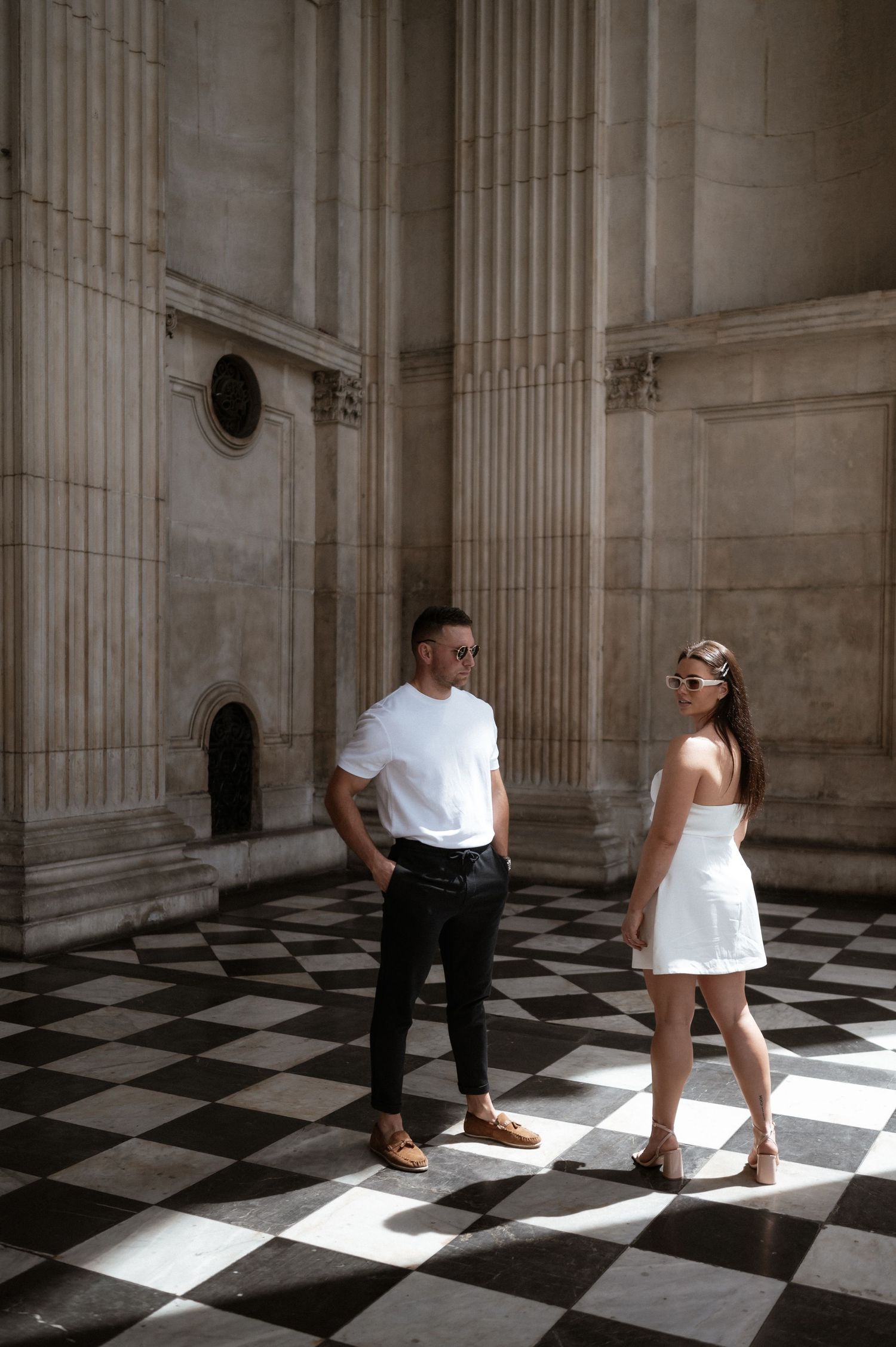 Couple poses on checkered floor inside historic building with classical columns.
