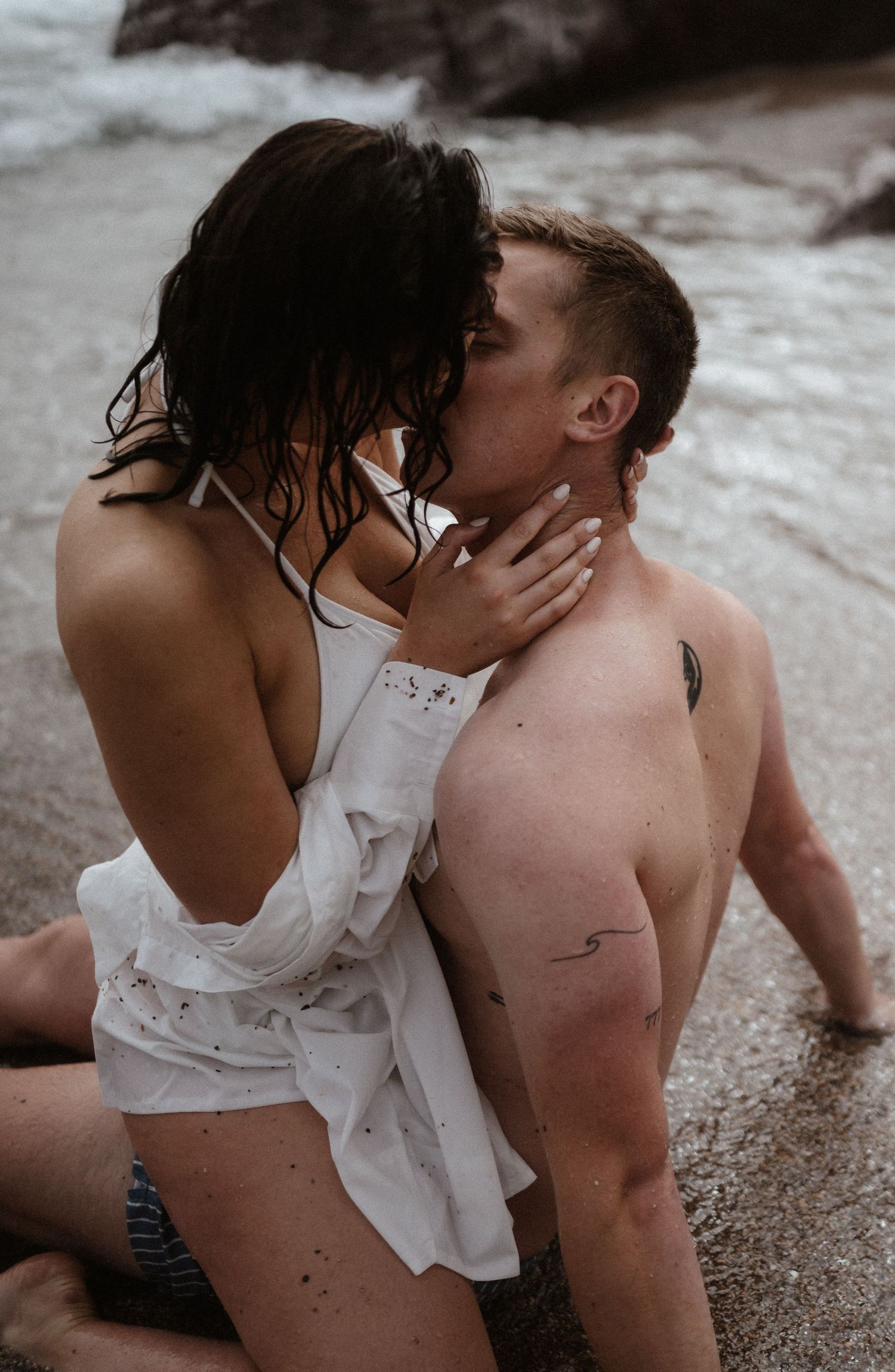 Intimate beach moment between couple in white clothing at waters edge.