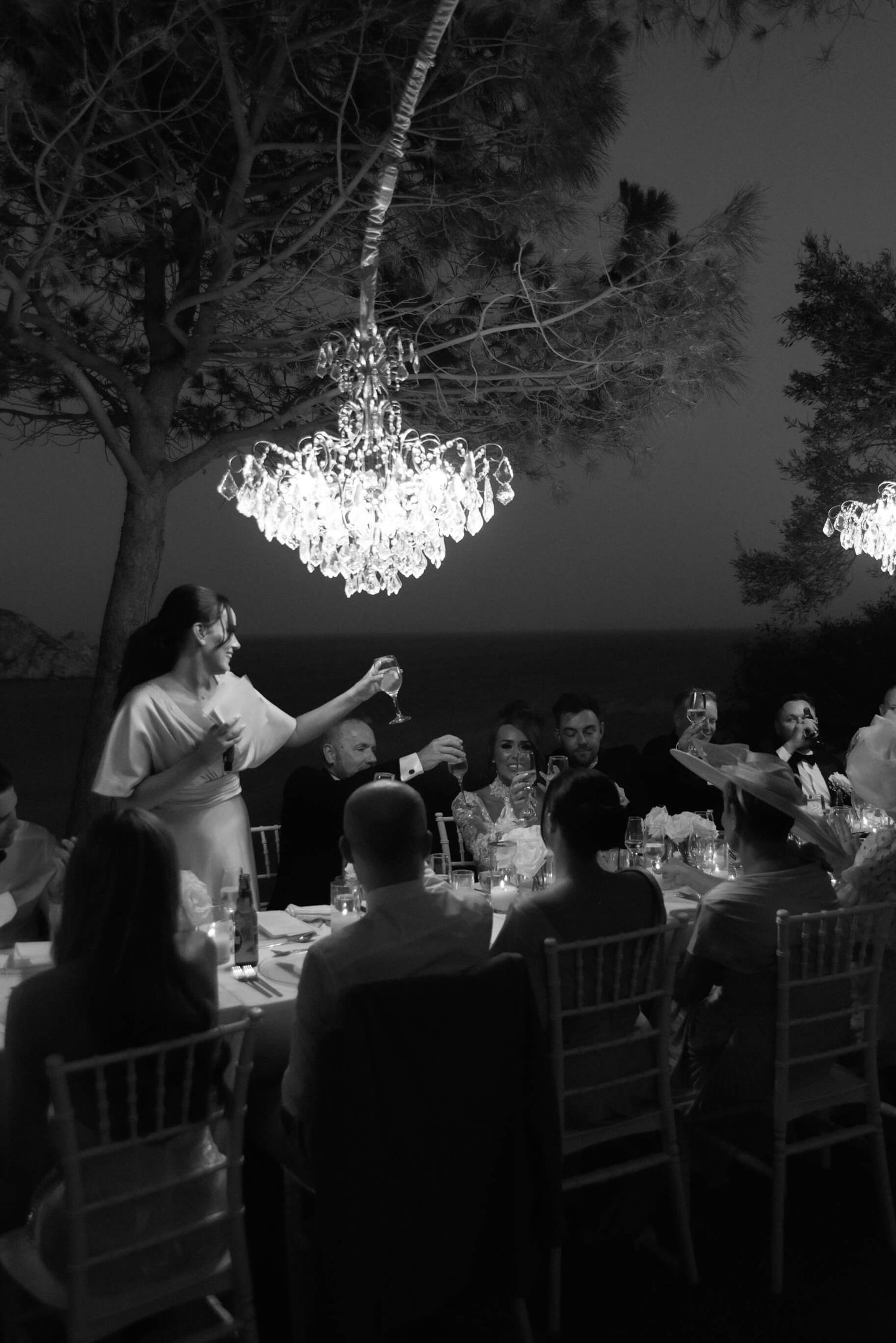 An elegant outdoor evening reception with crystal chandeliers hanging from trees.