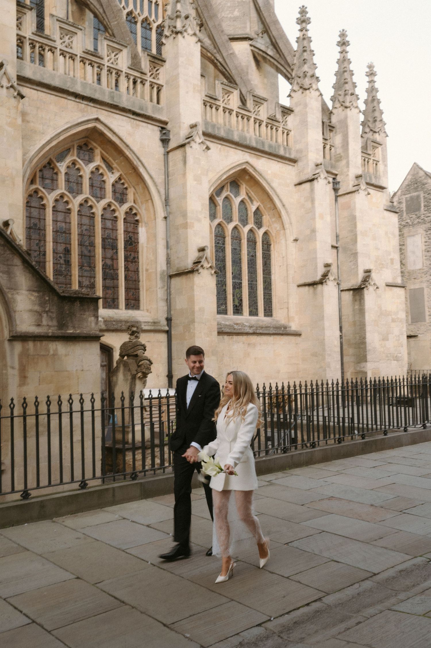 Couple walking together outside a historic Gothic church with ornate stone architecture and iron railings.