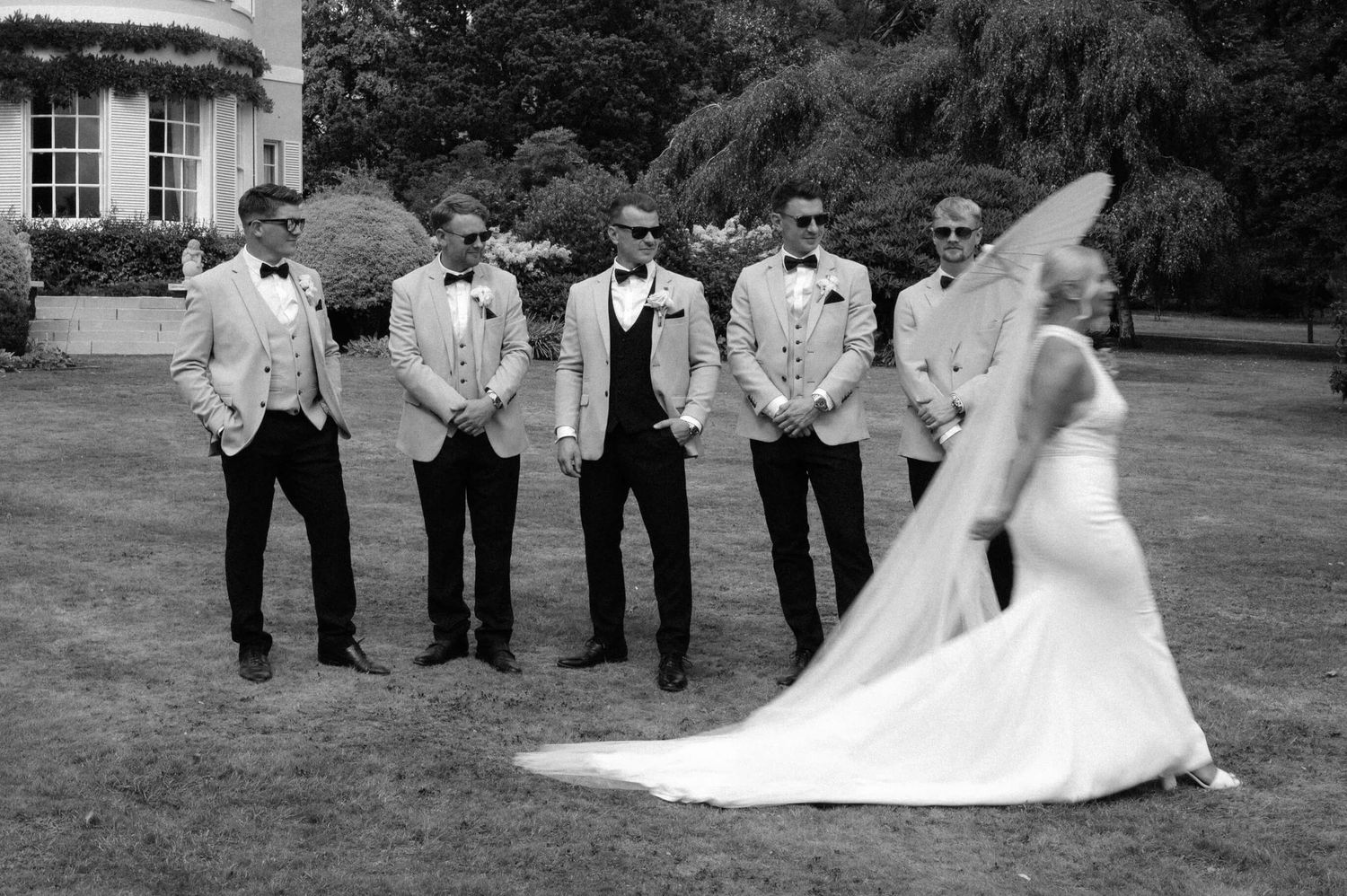 Wedding party poses on expansive lawn with long bridal train in black and white photography.