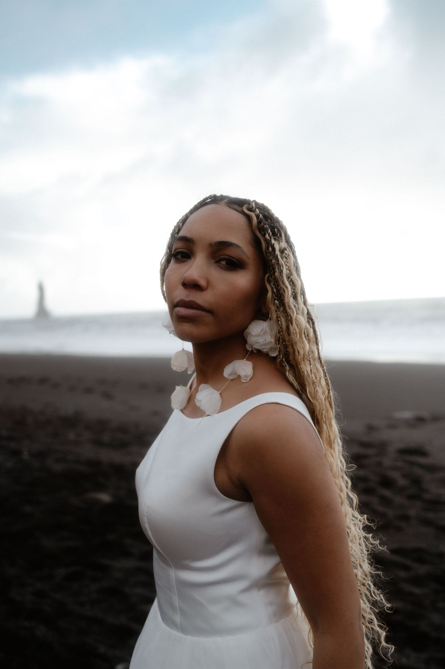 A woman in a white sleeveless dress poses outdoors against a moody sky in a series of dramatic portrait shots.