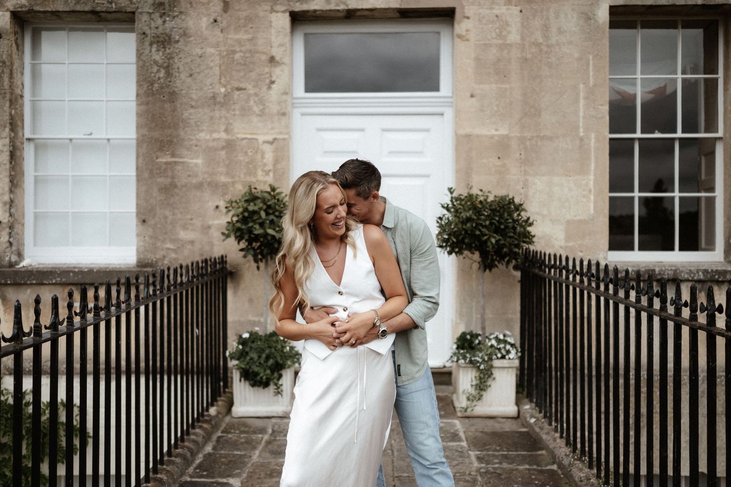 Tender embrace on classic stone steps with white dress and casual attire.