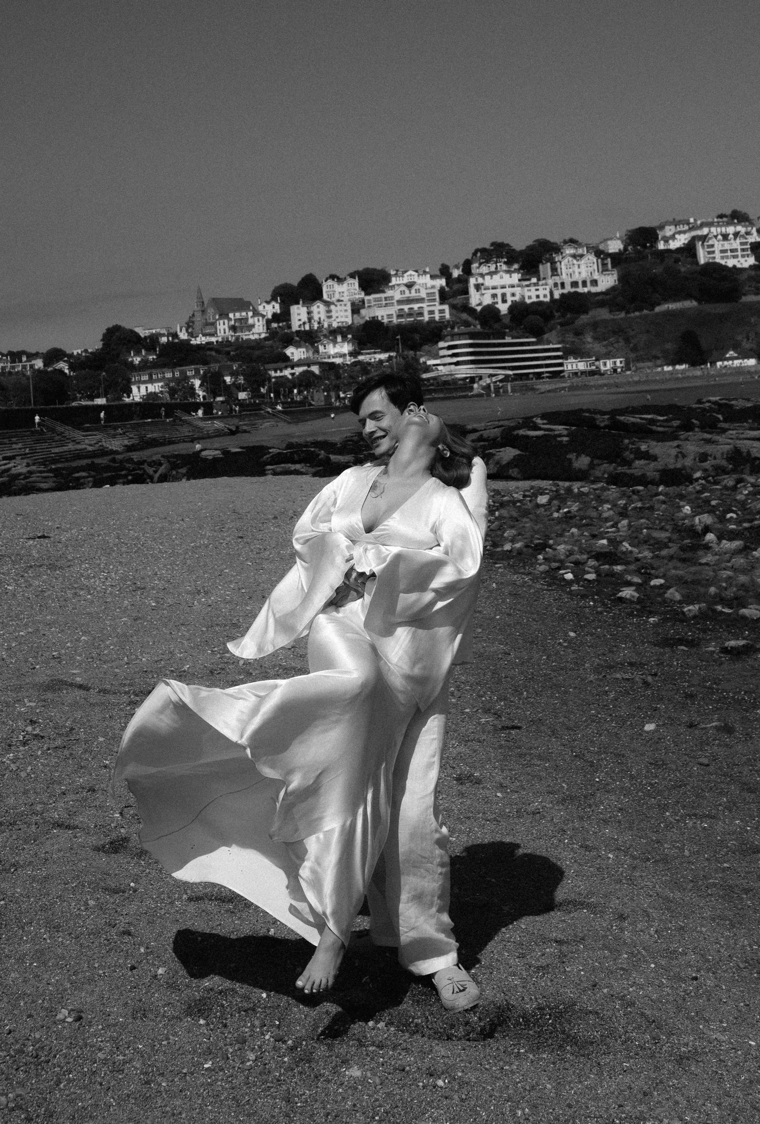 A sequence of black and white photos shows a figure in flowing white dress dancing gracefully on a rocky shoreline.