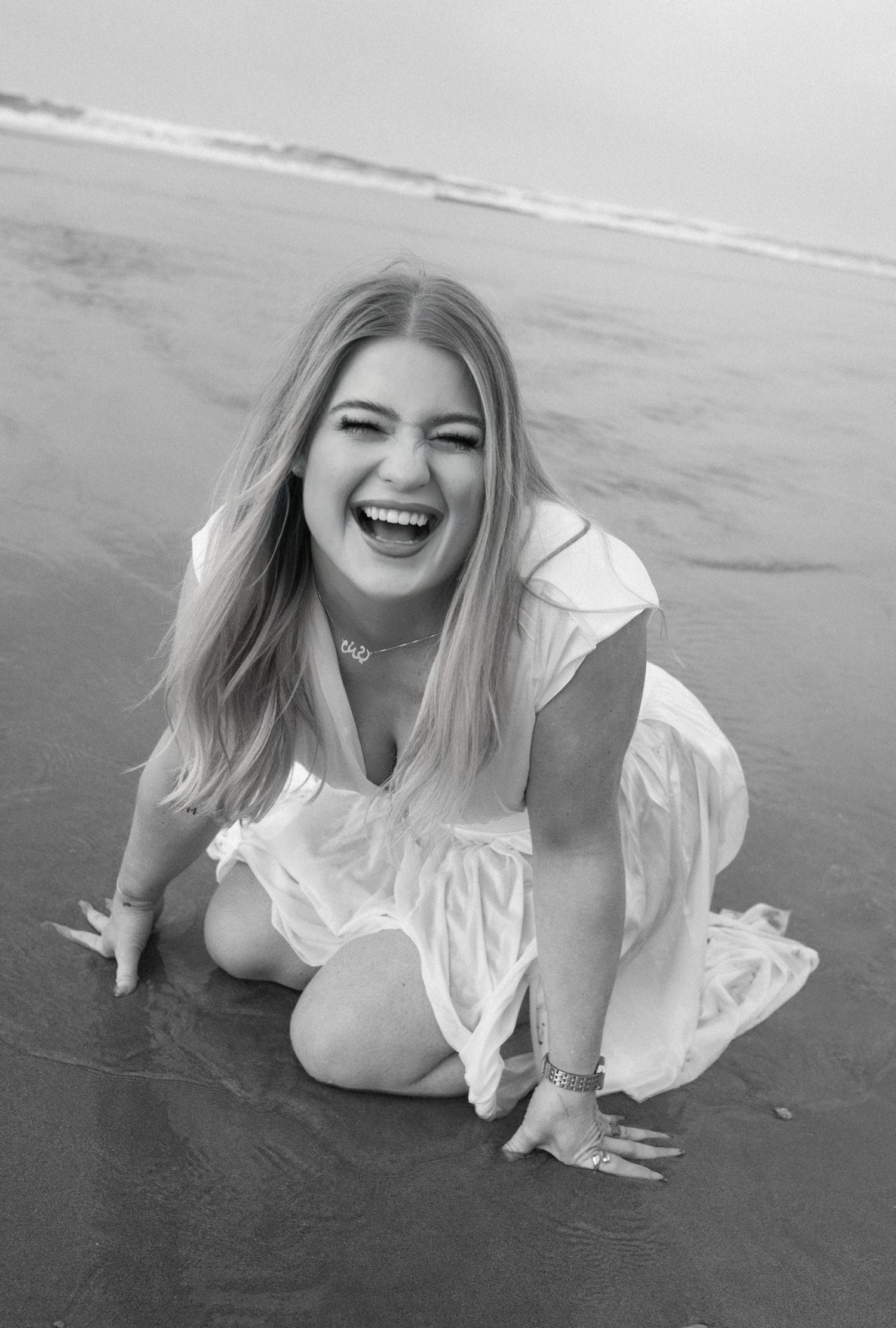 A person wearing a white dress lies on a sandy beach in a series of black and white artistic portraits.