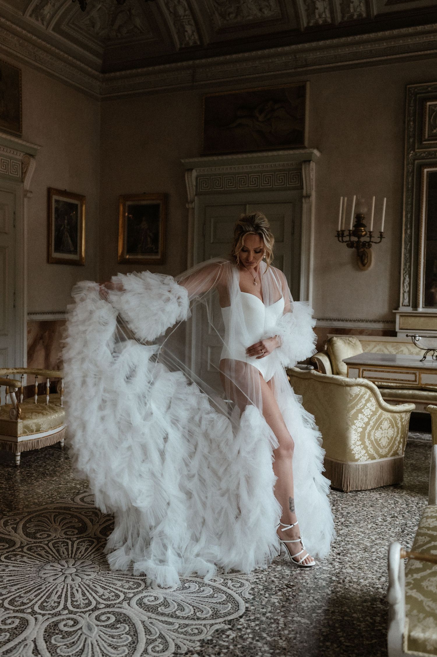 Dramatic bridal boudoir photo in an ornate room with a flowing white feathered gown.