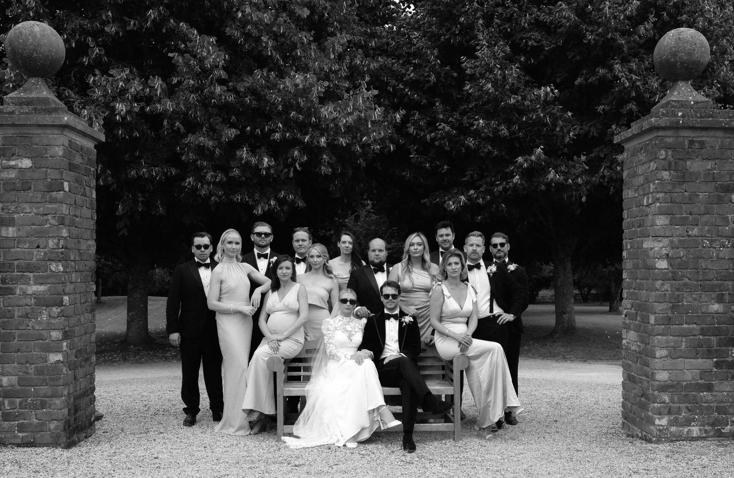 Wedding party poses for group photos against brick wall in black and white.