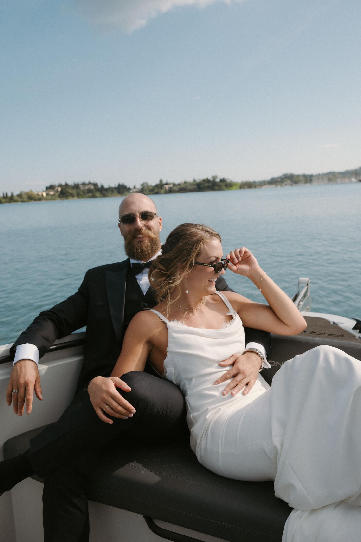 Newlyweds lounging together on a boat with a scenic lake and blue sky in the background.