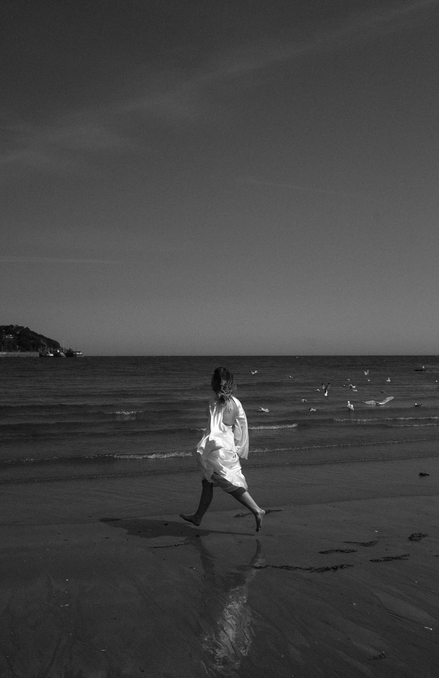 Silhouettes of figures in white clothing running along a beach at sunset with seagulls flying overhead.