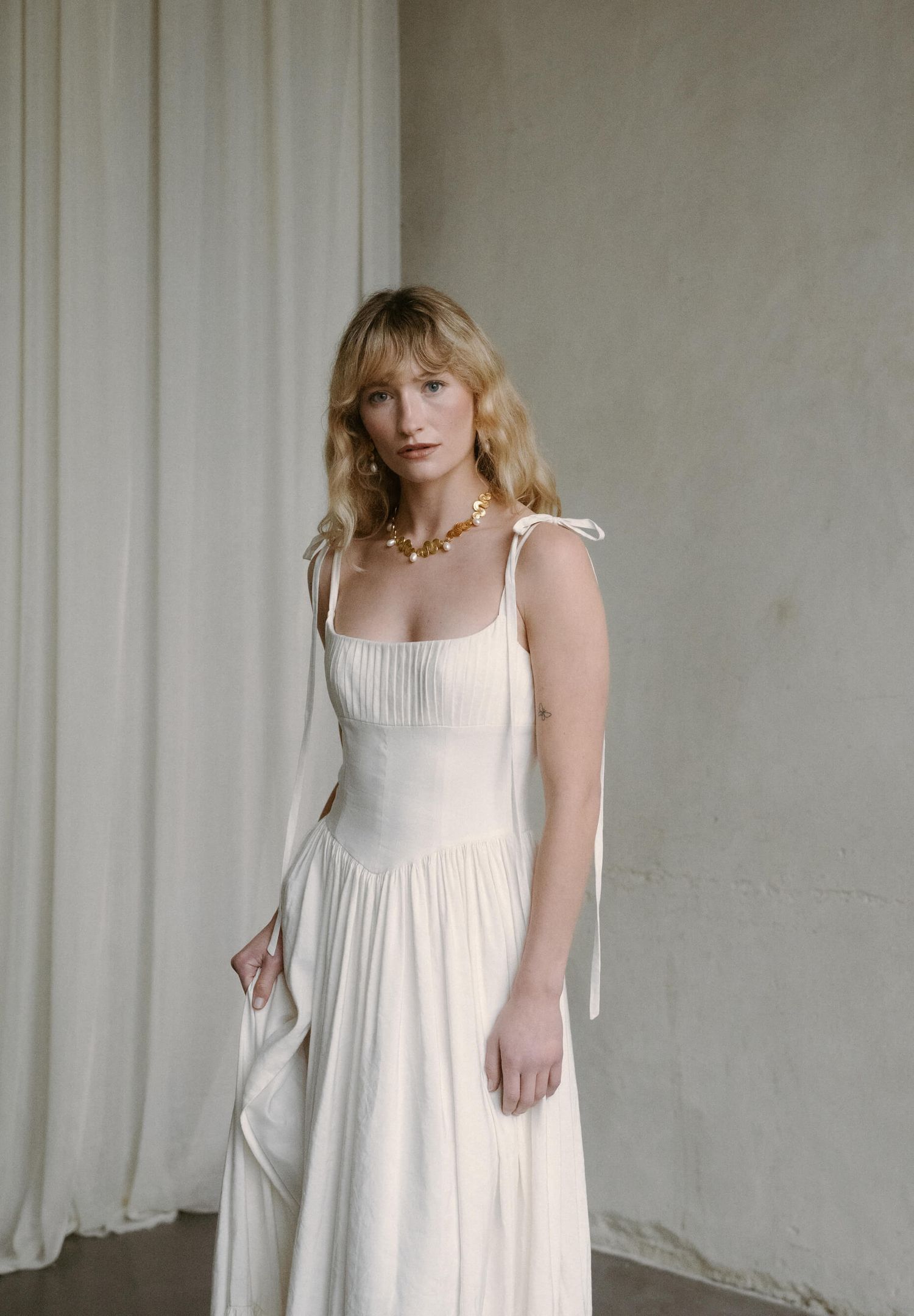 White empire waist dress with spaghetti straps photographed against neutral wall.