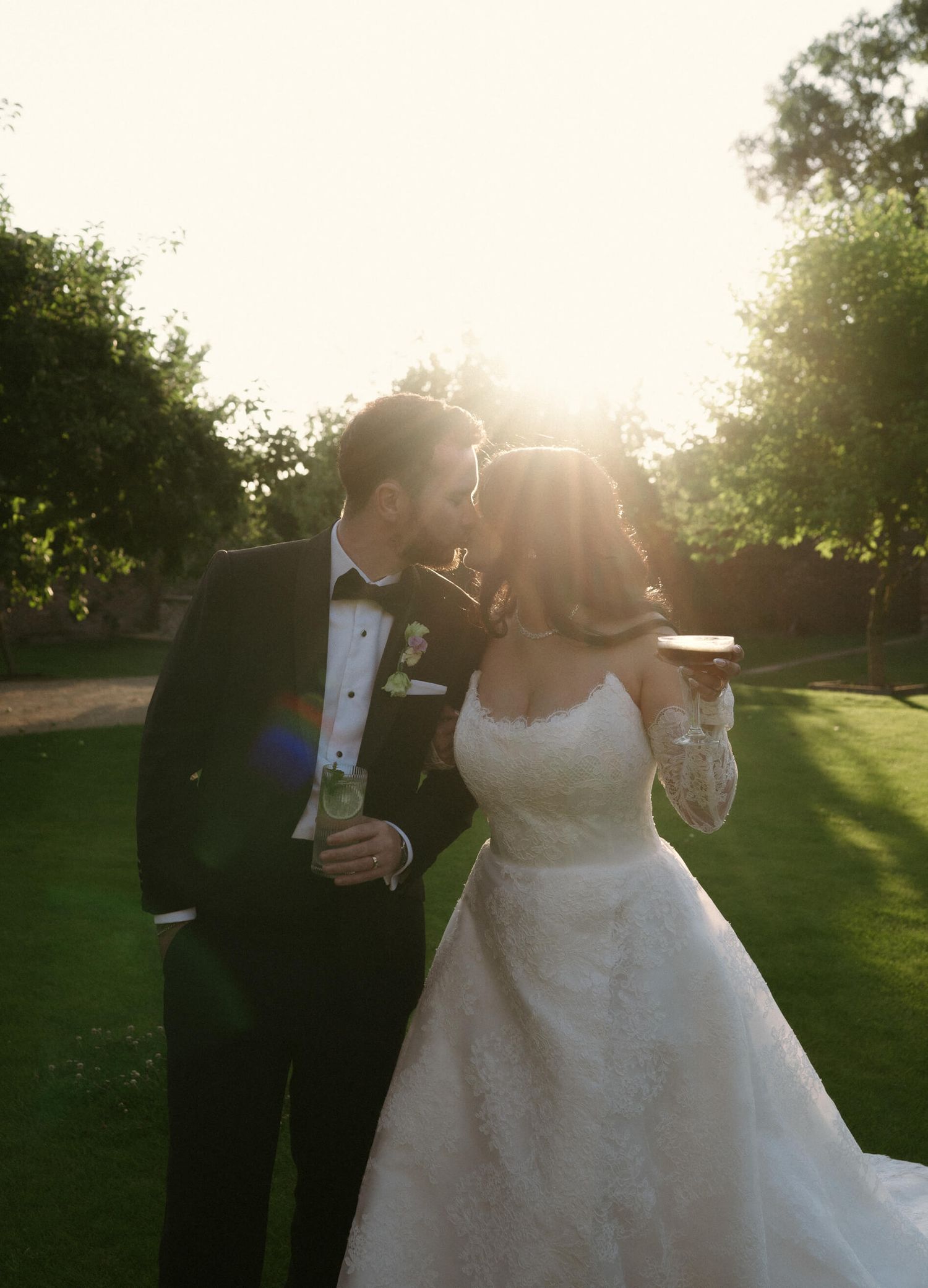 Wedding couple dances in golden sunset light on manicured garden lawn.