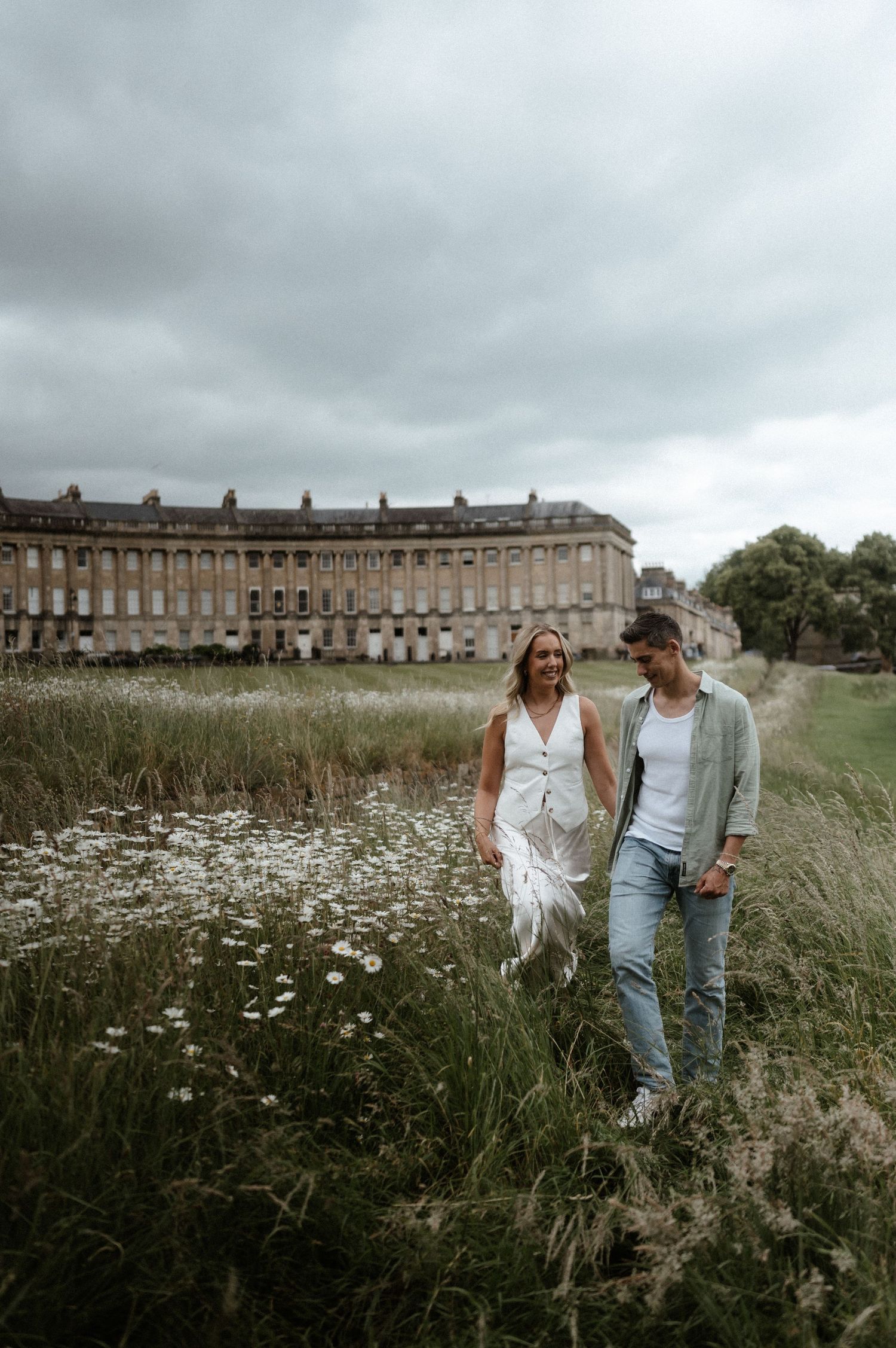 A couple walks through a wildflower meadow with the Royal Crescent in background.