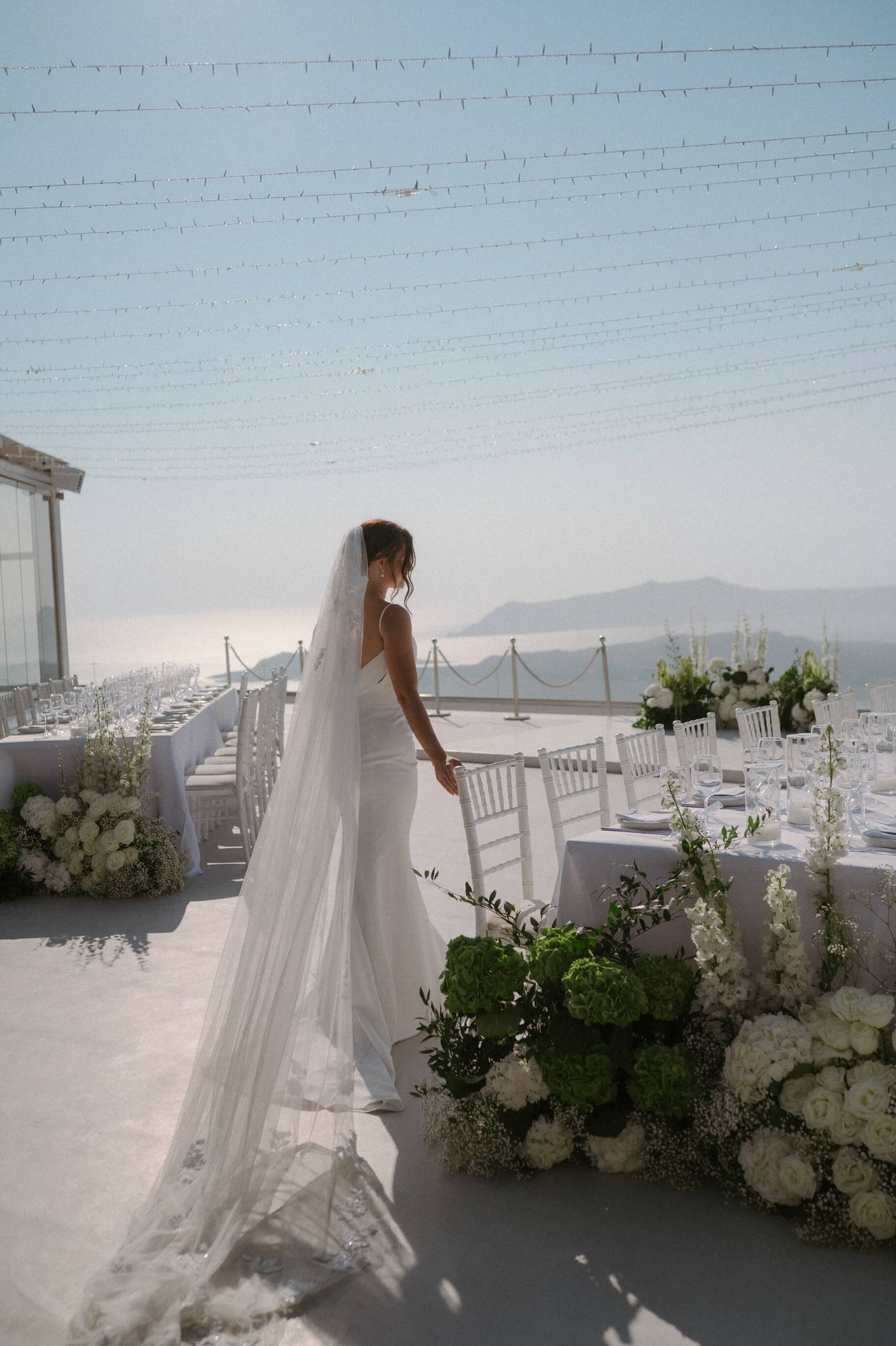 White floral decorations and string lights adorn a Mediterranean terrace with ocean views.