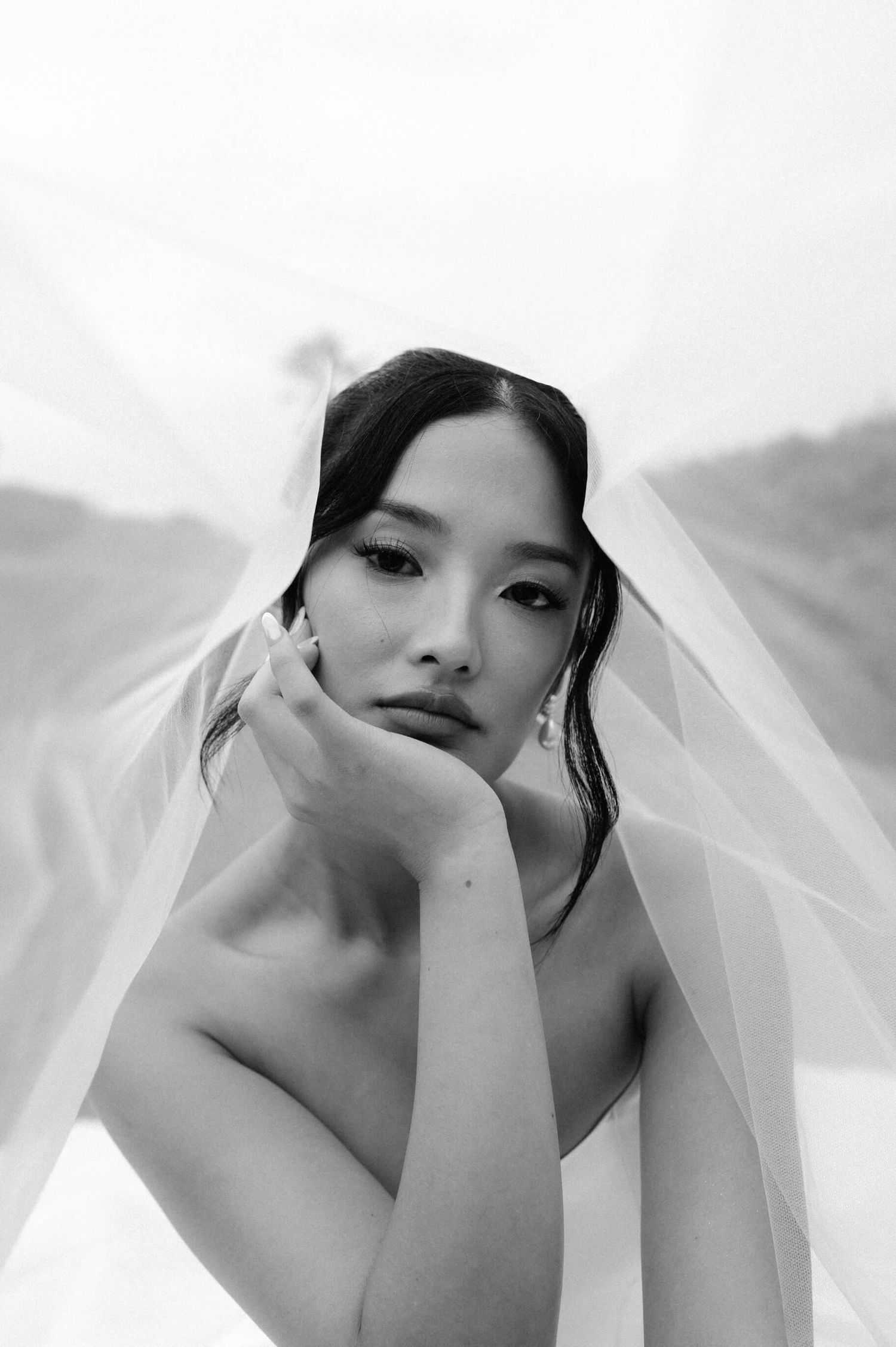 Artistic black and white bridal portrait with flowing veil creating ethereal atmosphere.