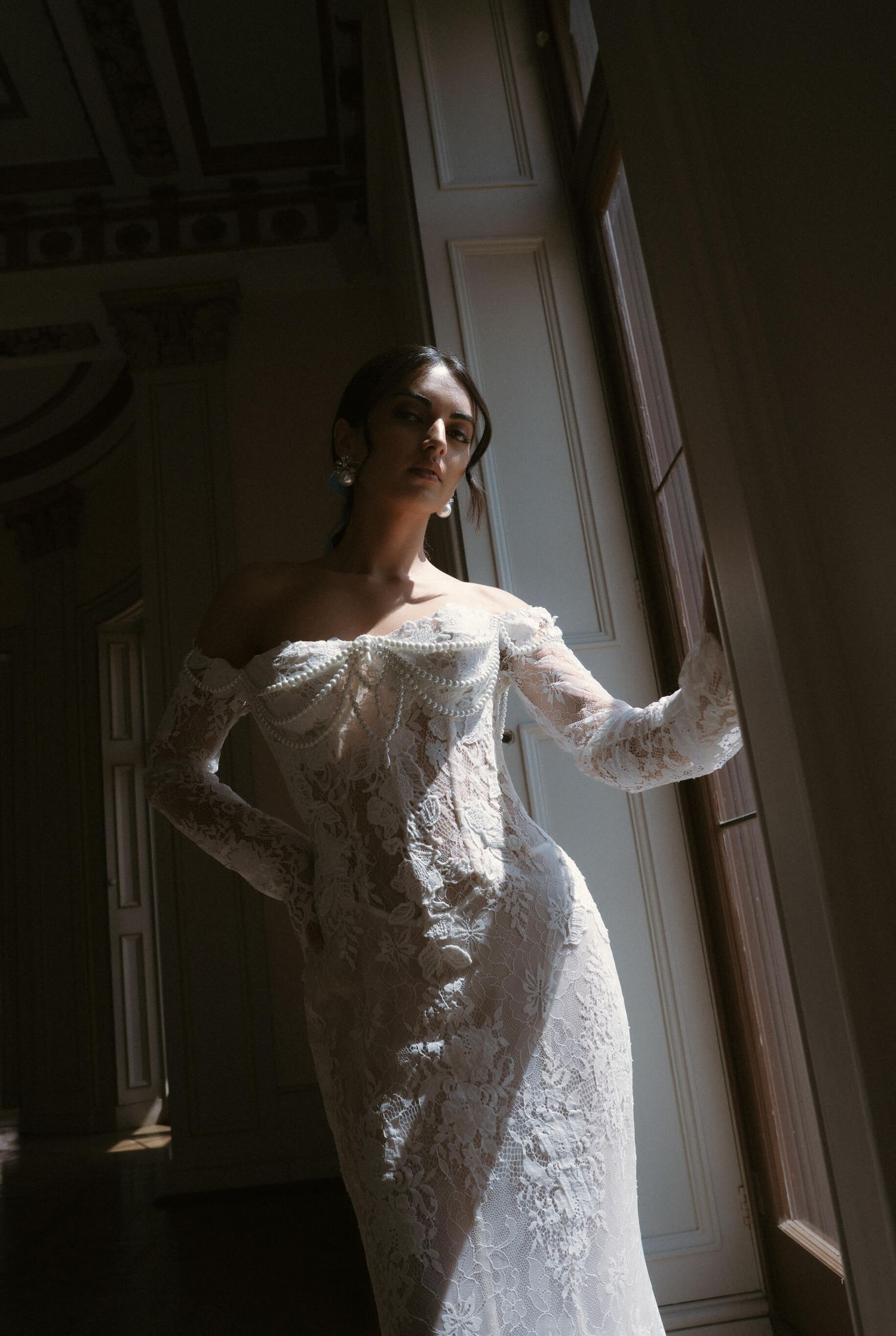 Delicate lace details of a wedding dress captured in dramatic window lighting.