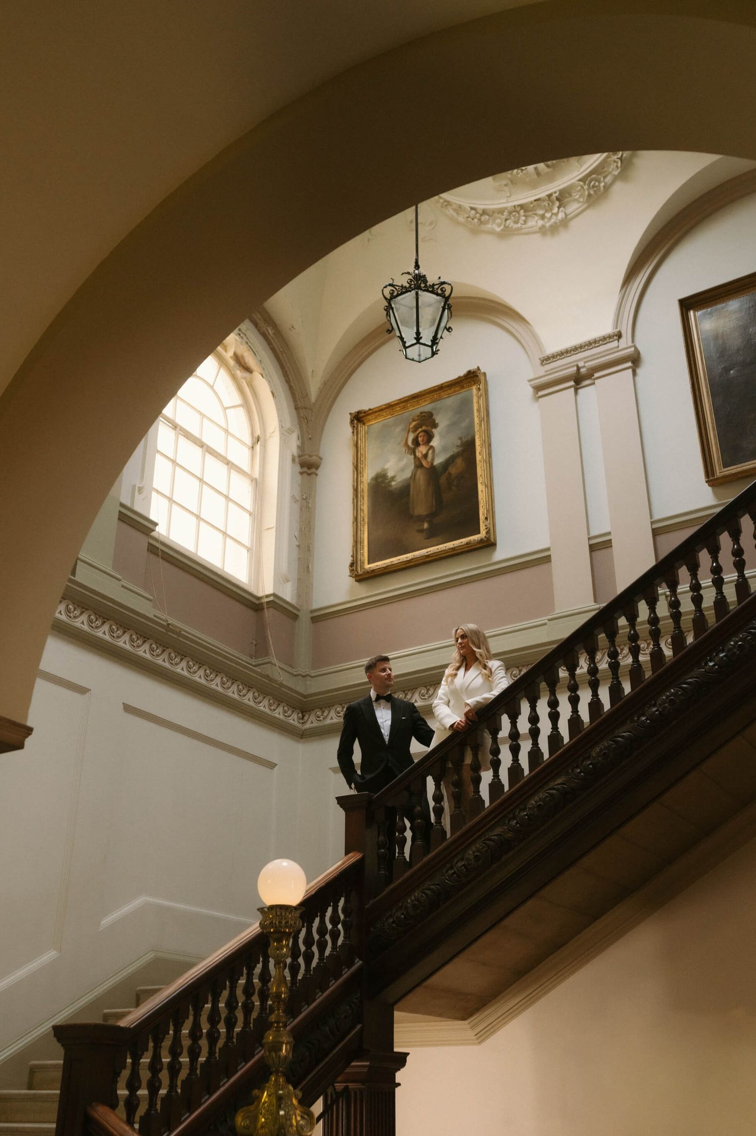 Elegant staircase scene in a historic building with arched windows and ornate architectural details.