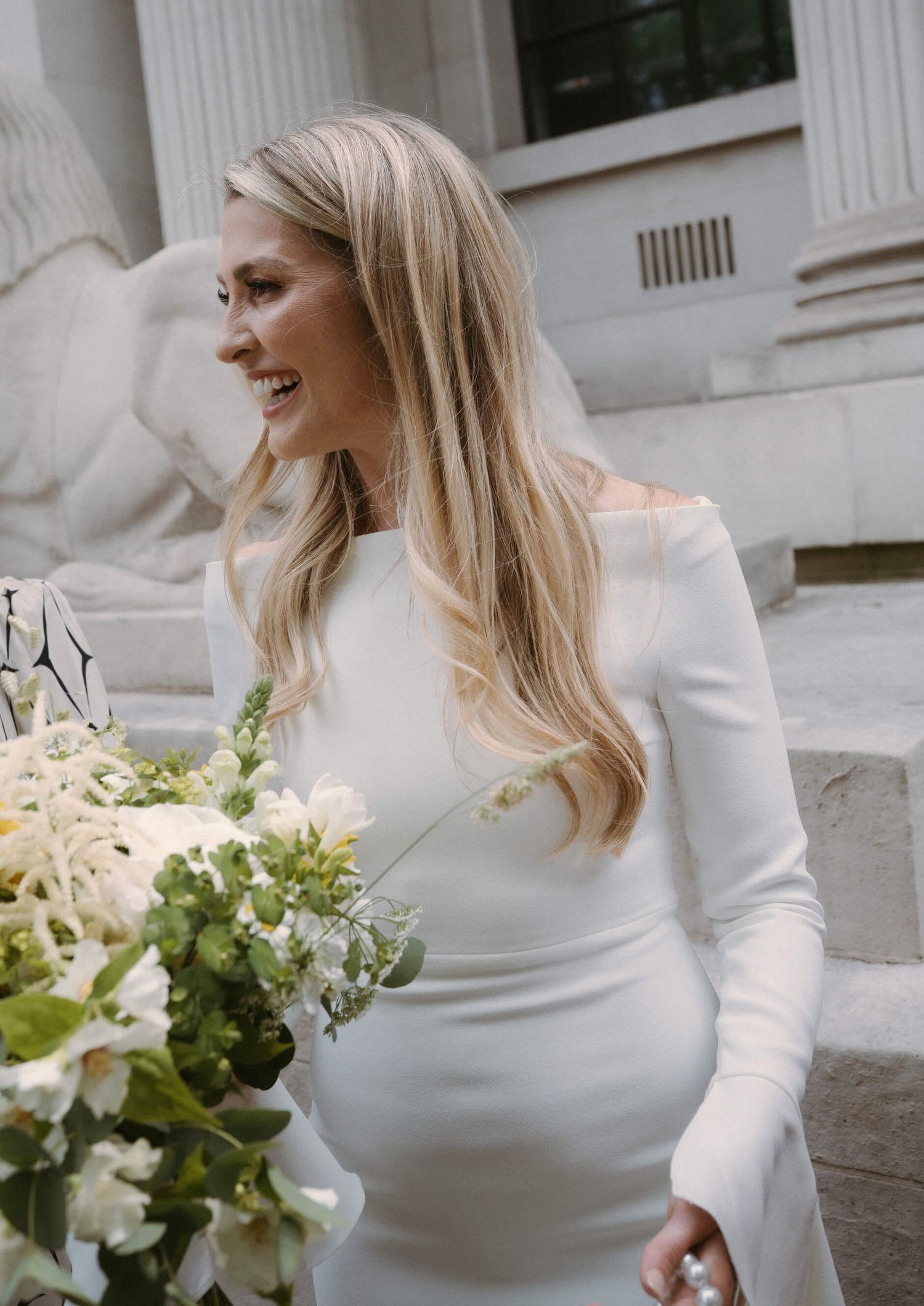 Bride in elegant white long-sleeved dress holding a delicate bouquet of flowers.