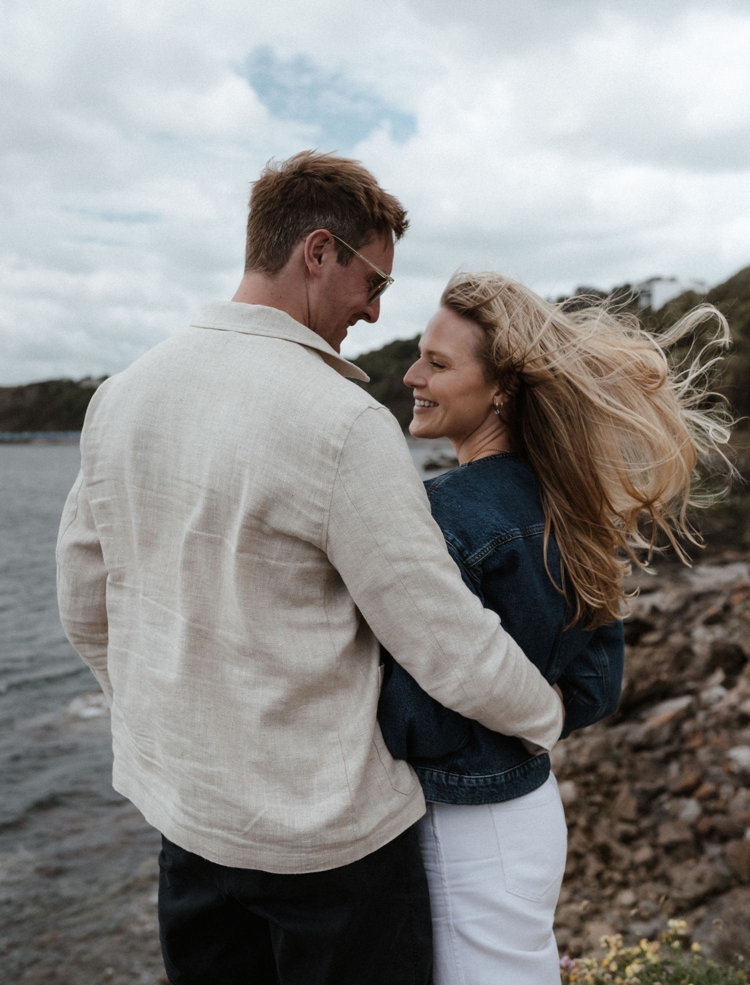 Romantic coastal moment with couple embracing against dramatic ocean backdrop.